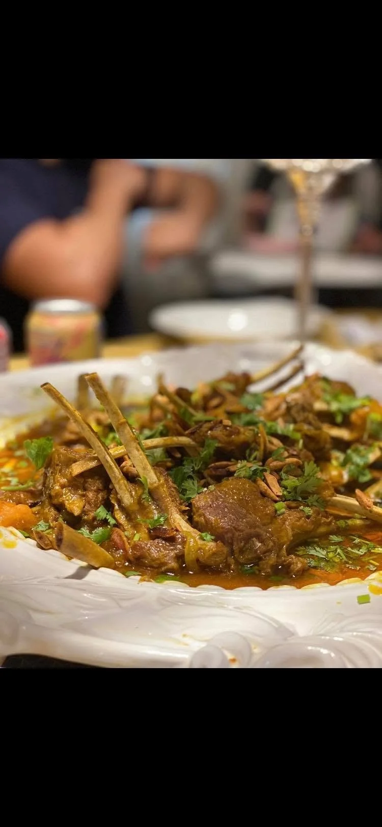 Close-up of a dish with cooked lamb chops garnished with green herbs, served on a decorative white platter.