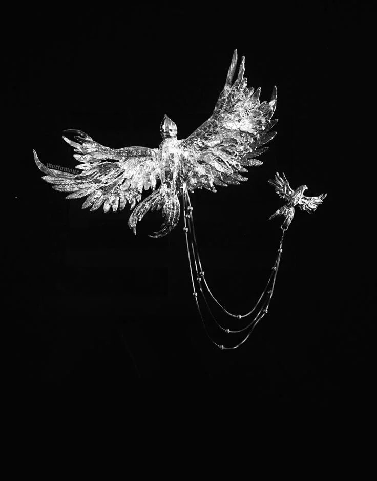 A decorative glass sculpture of two birds with outstretched wings connected by hanging chains, set against a black background.