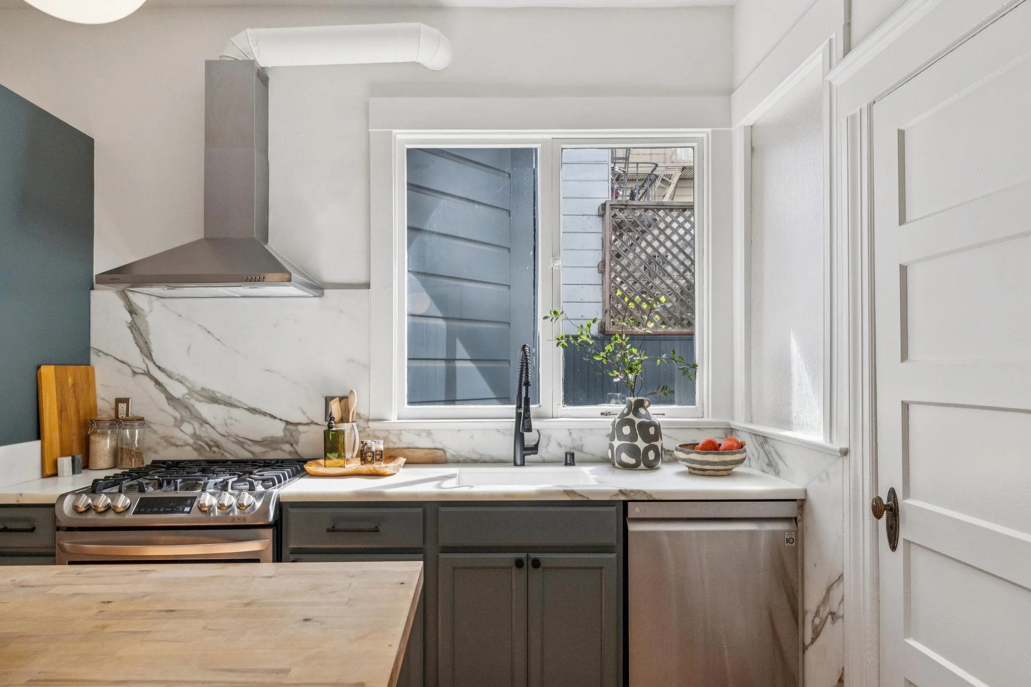 Kitchen with white marble backsplash, gray cabinets, window with view of outdoor balcony, and wooden countertop.