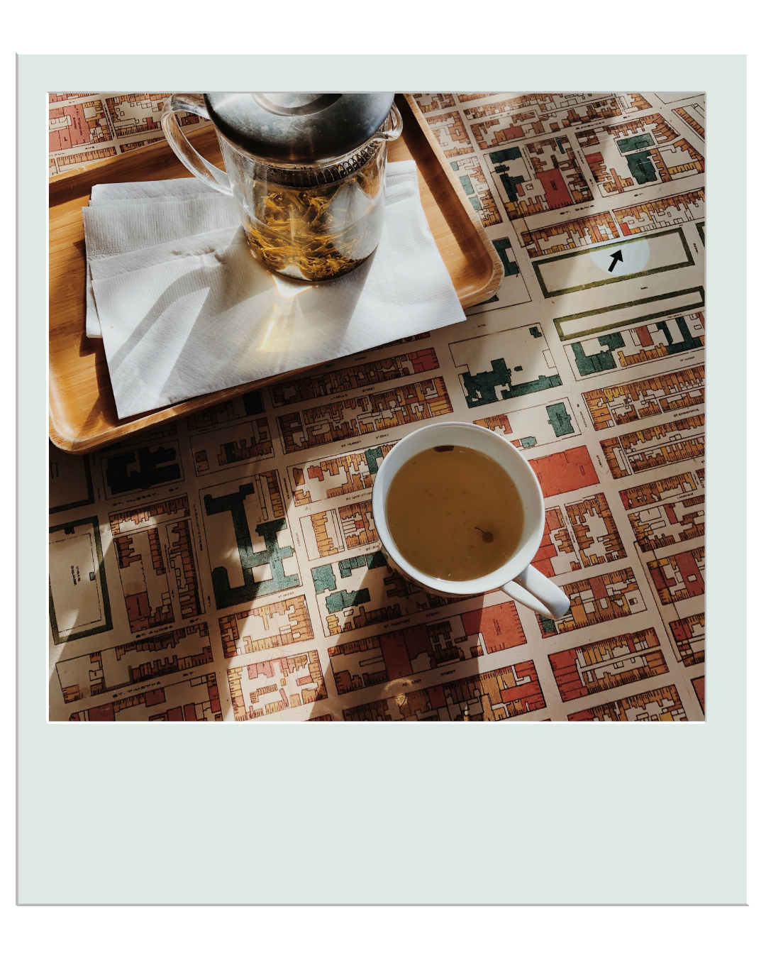 Une tasse de soupe et une théière avec du thé sur une table recouverte d'un plan de ville, avec des ombres qui tombent sur la table.