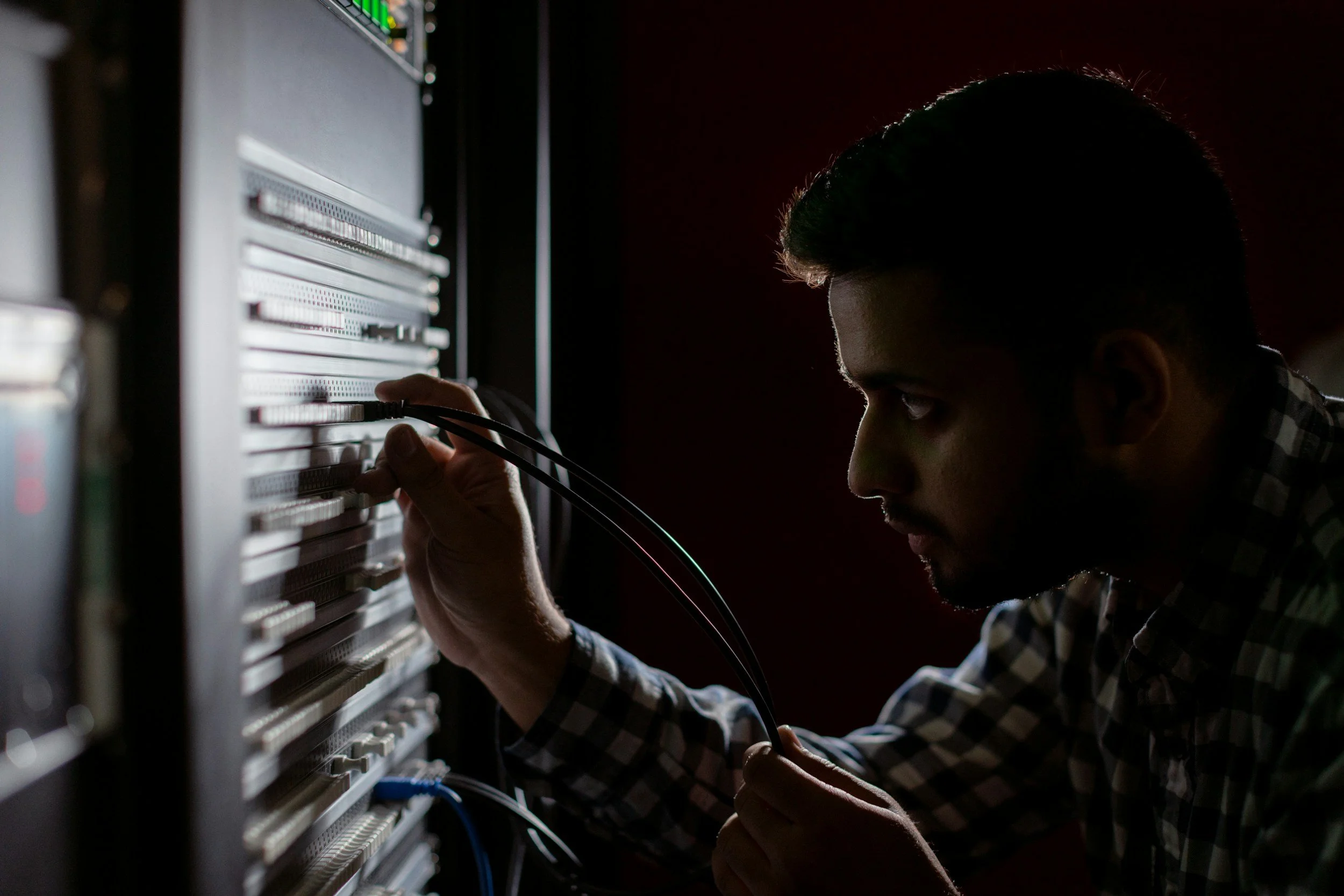 A man working on an electronic server or network equipment, connecting or repairing cables.