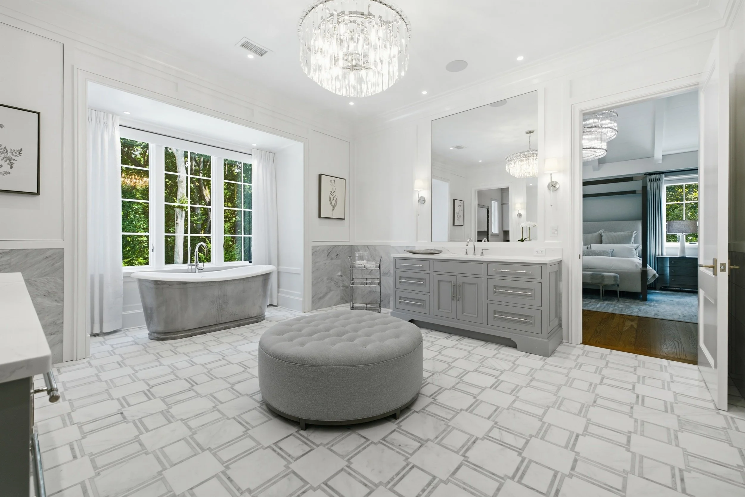 Bright and airy bathroom with white walls and cabinetry, large window with white curtains, freestanding bathtub, and modern lighting fixtures.
