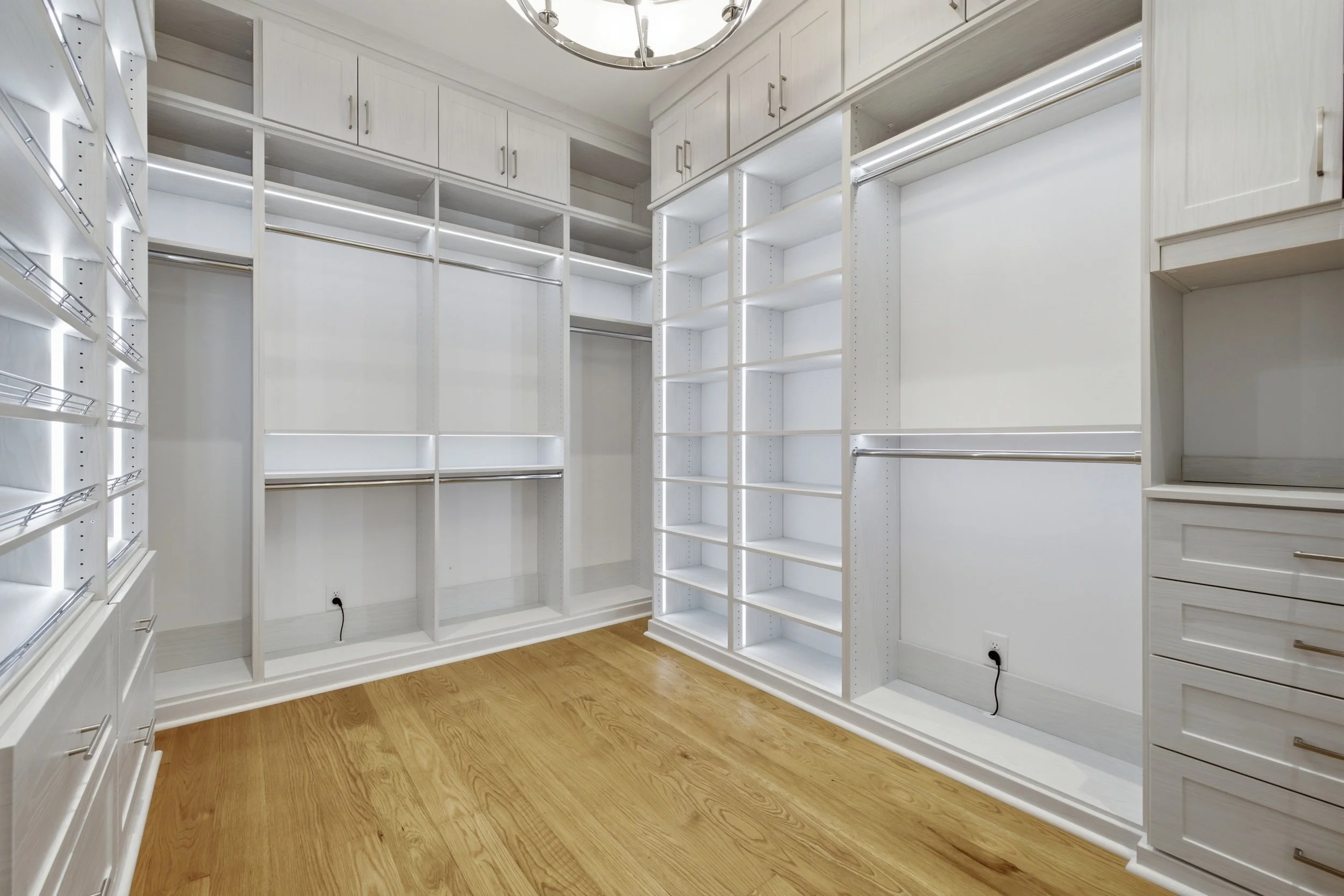 Empty walk-in closet with white shelves, cabinetry, and wood flooring.