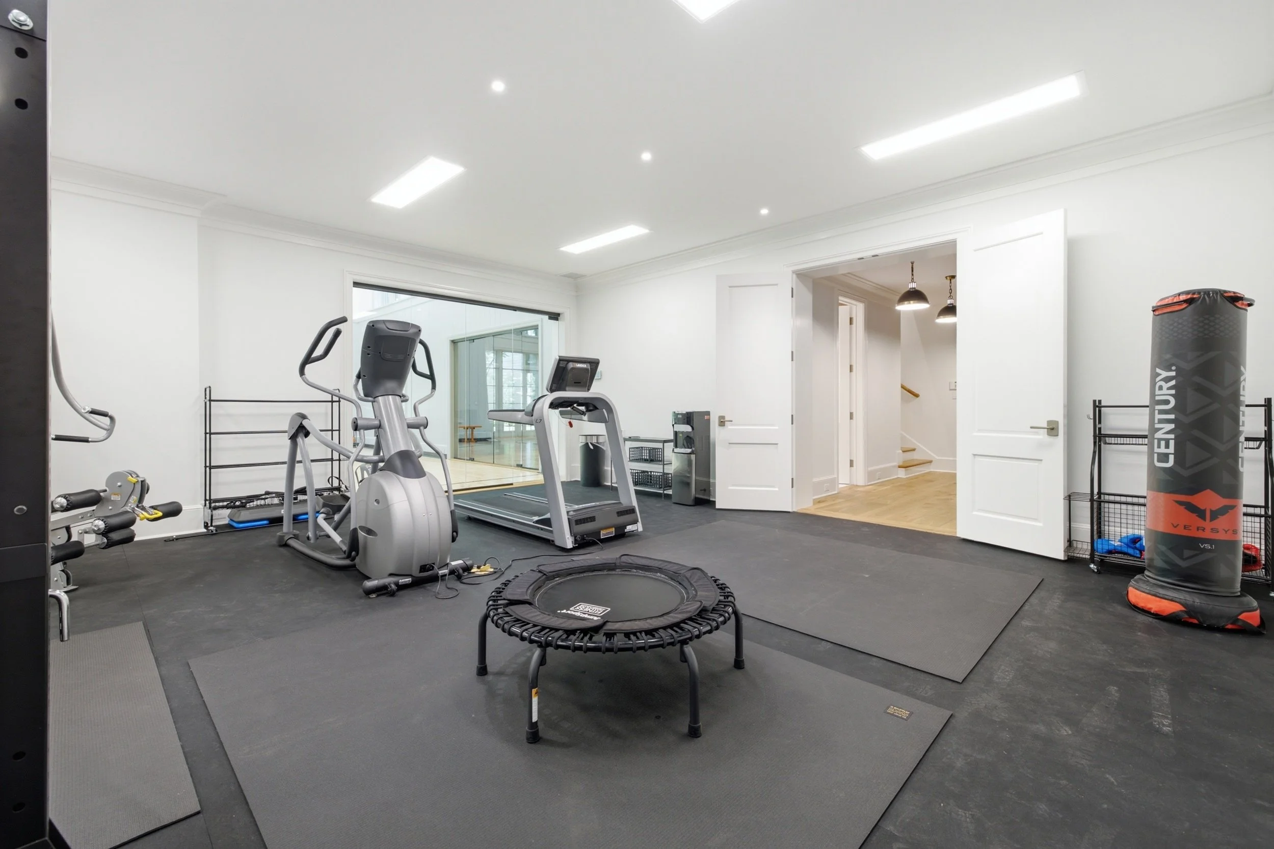 Home gym with fitness equipment, treadmill, exercise bikes, punching bag, small trampoline, and workout mats.