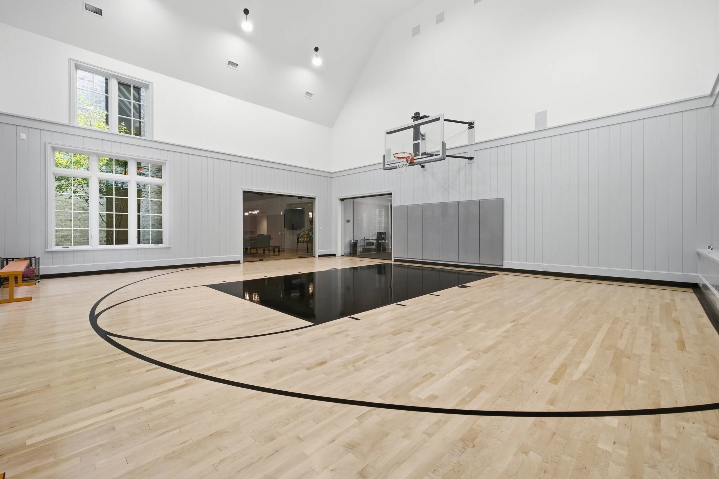 Empty indoor basketball court with a hoop, large windows, and natural light.