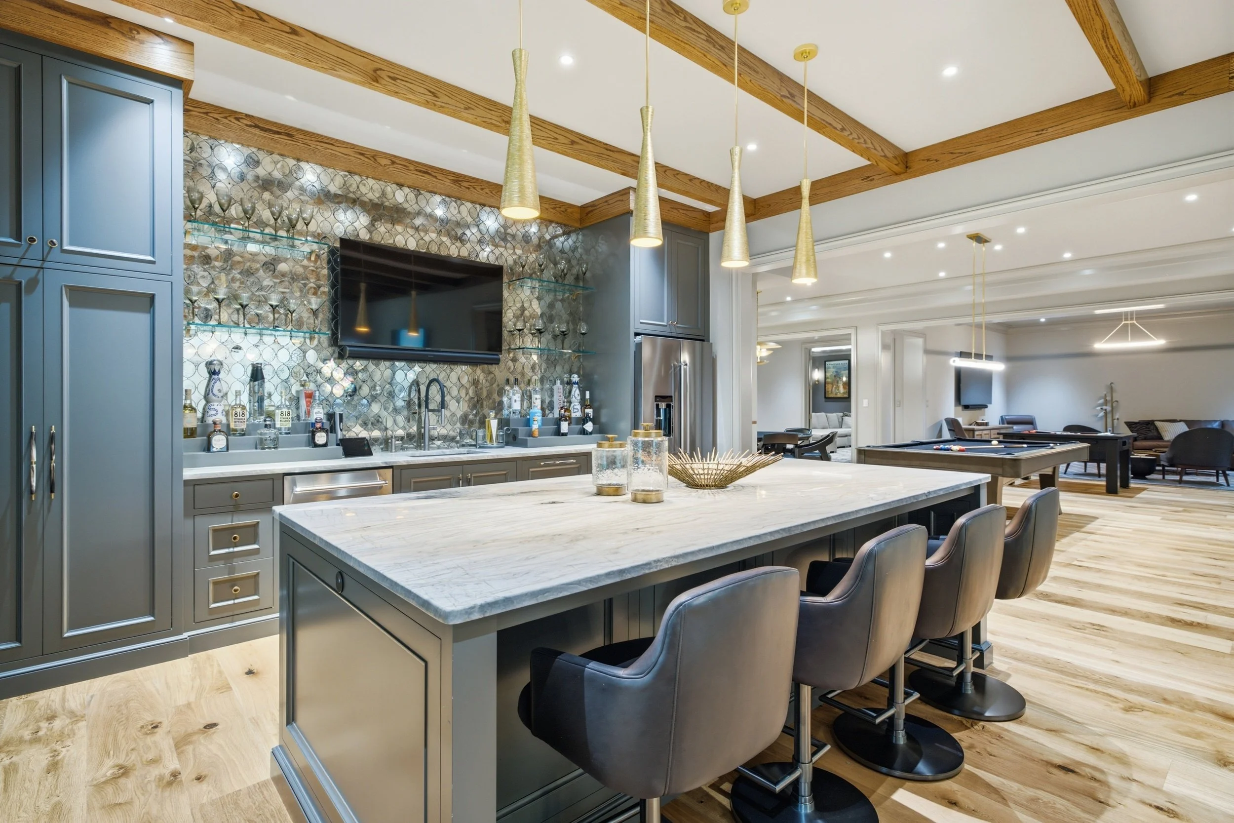 Modern open-concept kitchen with gray cabinetry, white marble island, gold pendant lights, and a living area with couches and a pool table.