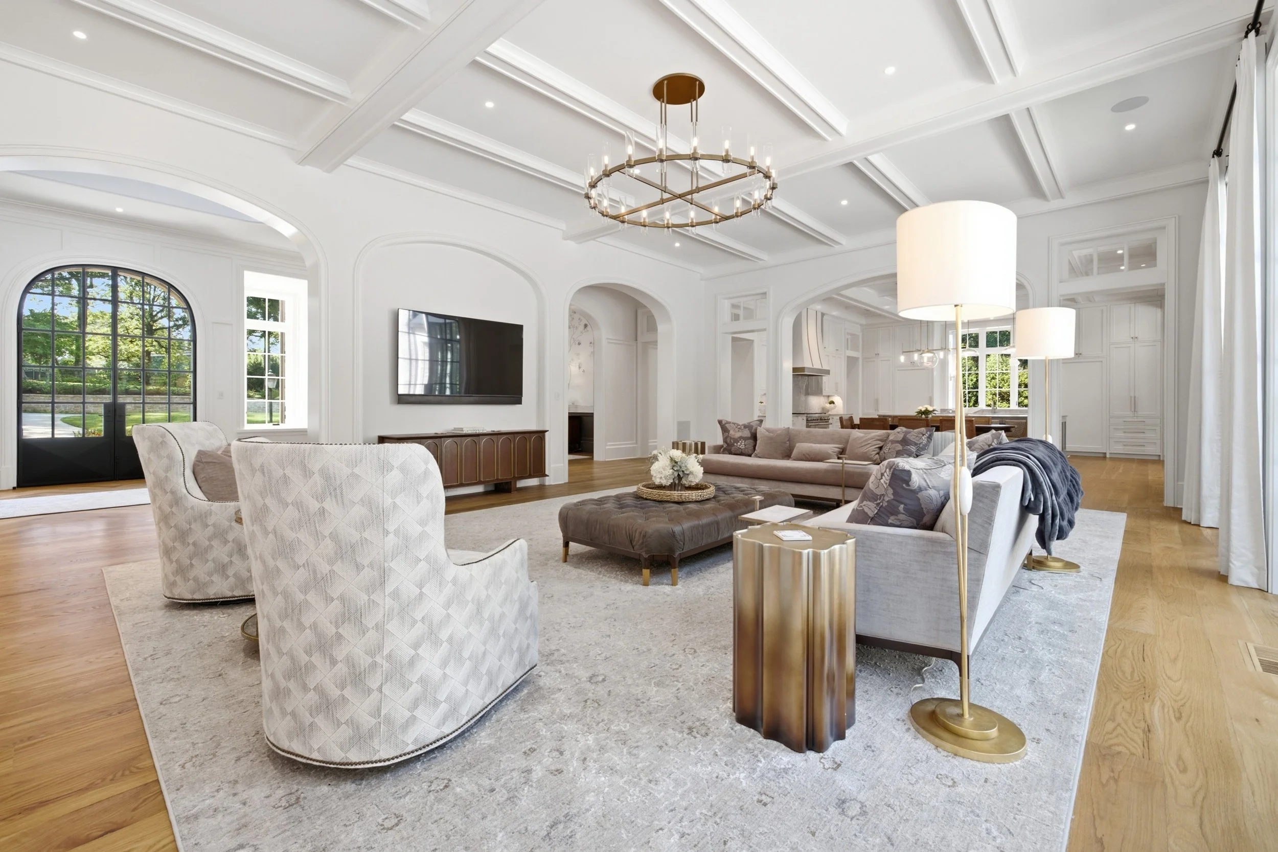 Elegant living room with white coffered ceiling, chandelier, large windows, and comfortable seating including a beige sofa and patterned armchairs.