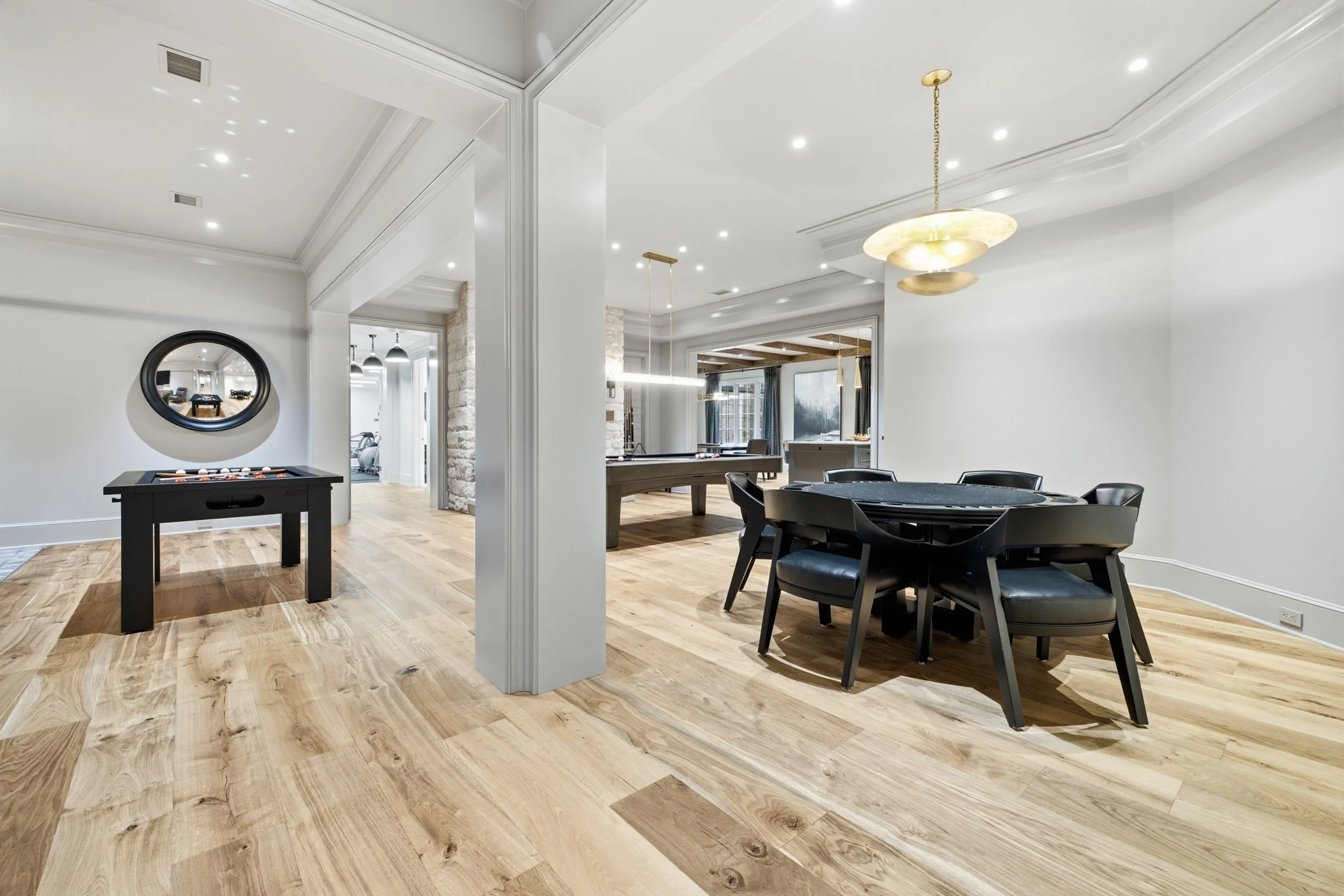 Modern open-concept living space with hardwood floors, a round black dining table with black chairs, a billiards table, contemporary light fixtures, and white walls with crown molding.