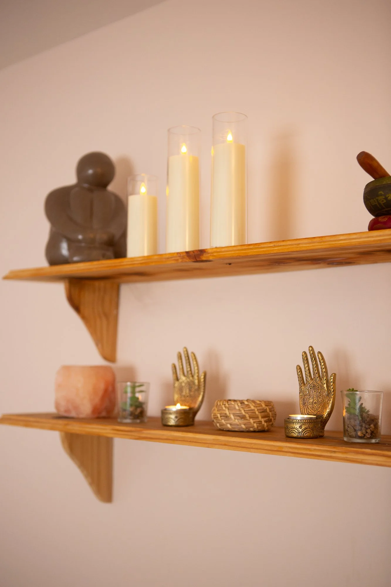 Two wooden shelves mounted on a wall, decorated with candles, sculptures, and decorative objects, creating a cozy and artistic display. One of the treatment rooms at Mothers Inc, East Dulwich.