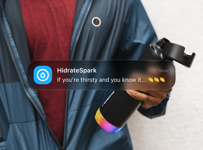 Person in a dark jacket holding a black smart water bottle with a colorful base, overlaid by a HidrateSpark hydration notification.