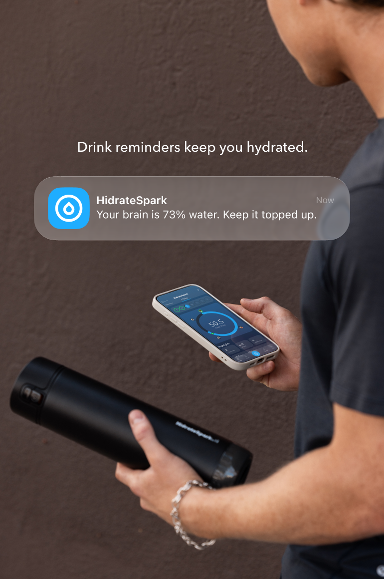 Person holding a HydrateSpark smart water bottle and smartphone displaying a hydration reminder notification.