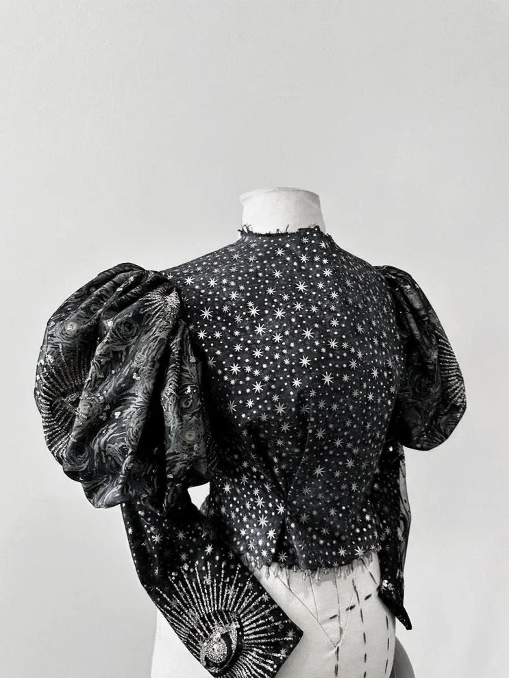 Black jacket with star and celestial patterns on a mannequin, featuring large puff sleeves.
