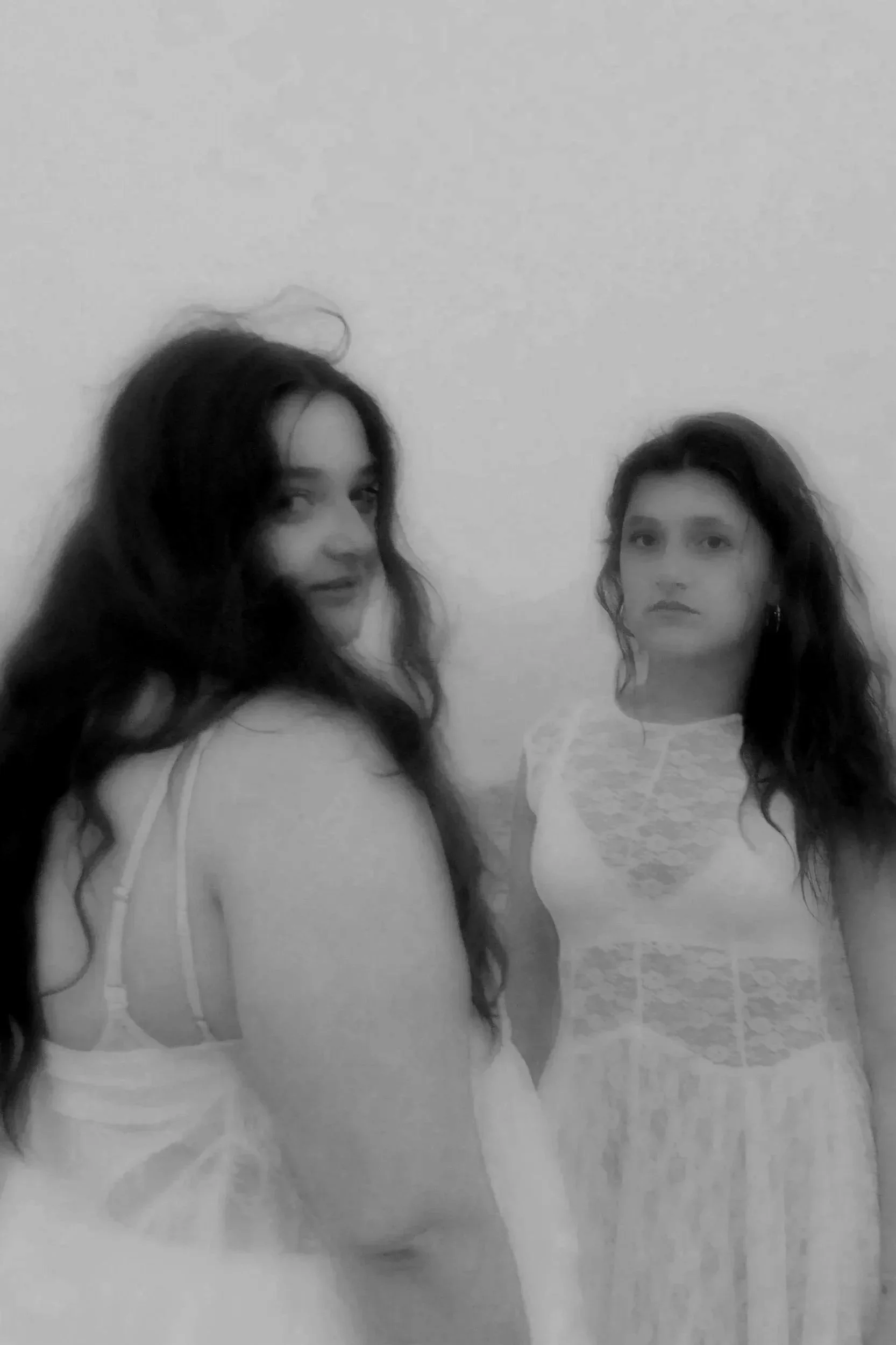 Black and white photo of two young women standing against a plain wall, both looking at the camera with neutral expressions.