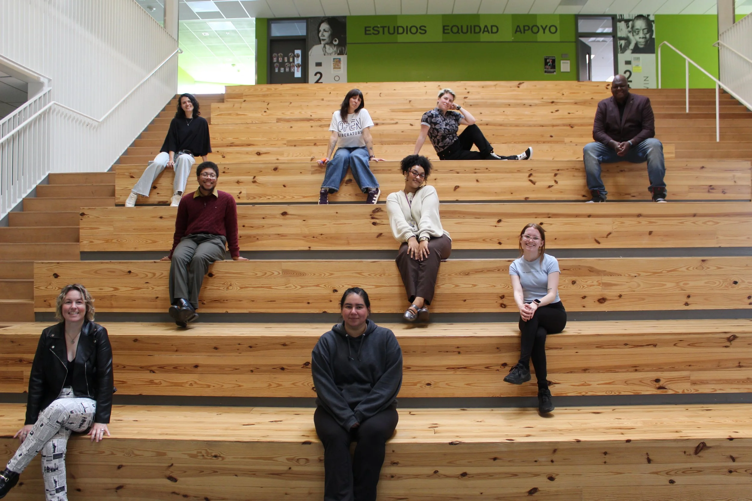 Students and community members seated on wide wooden steps in a school common space