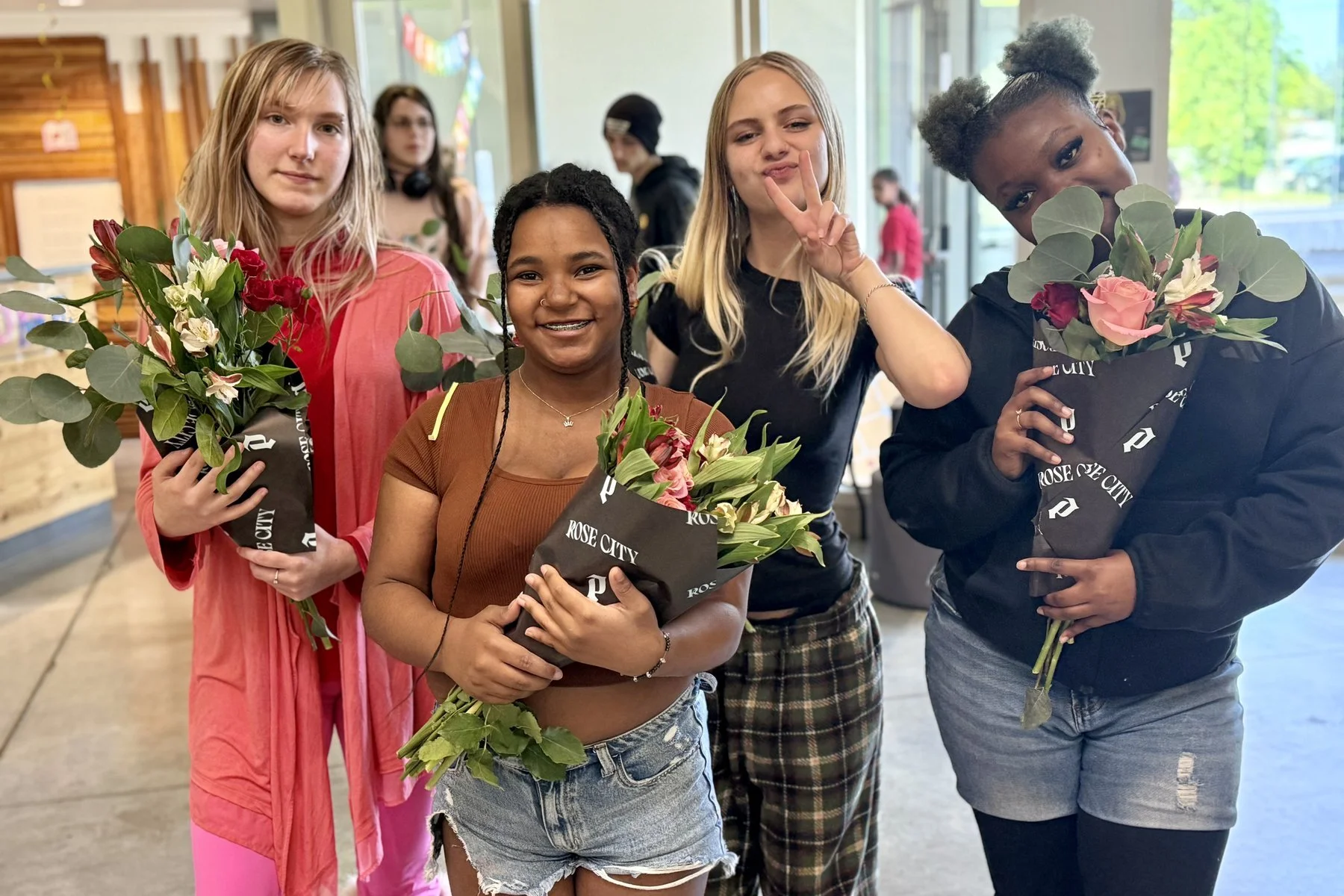 Open School East students smiling and holding bouquets of flowers at a celebration