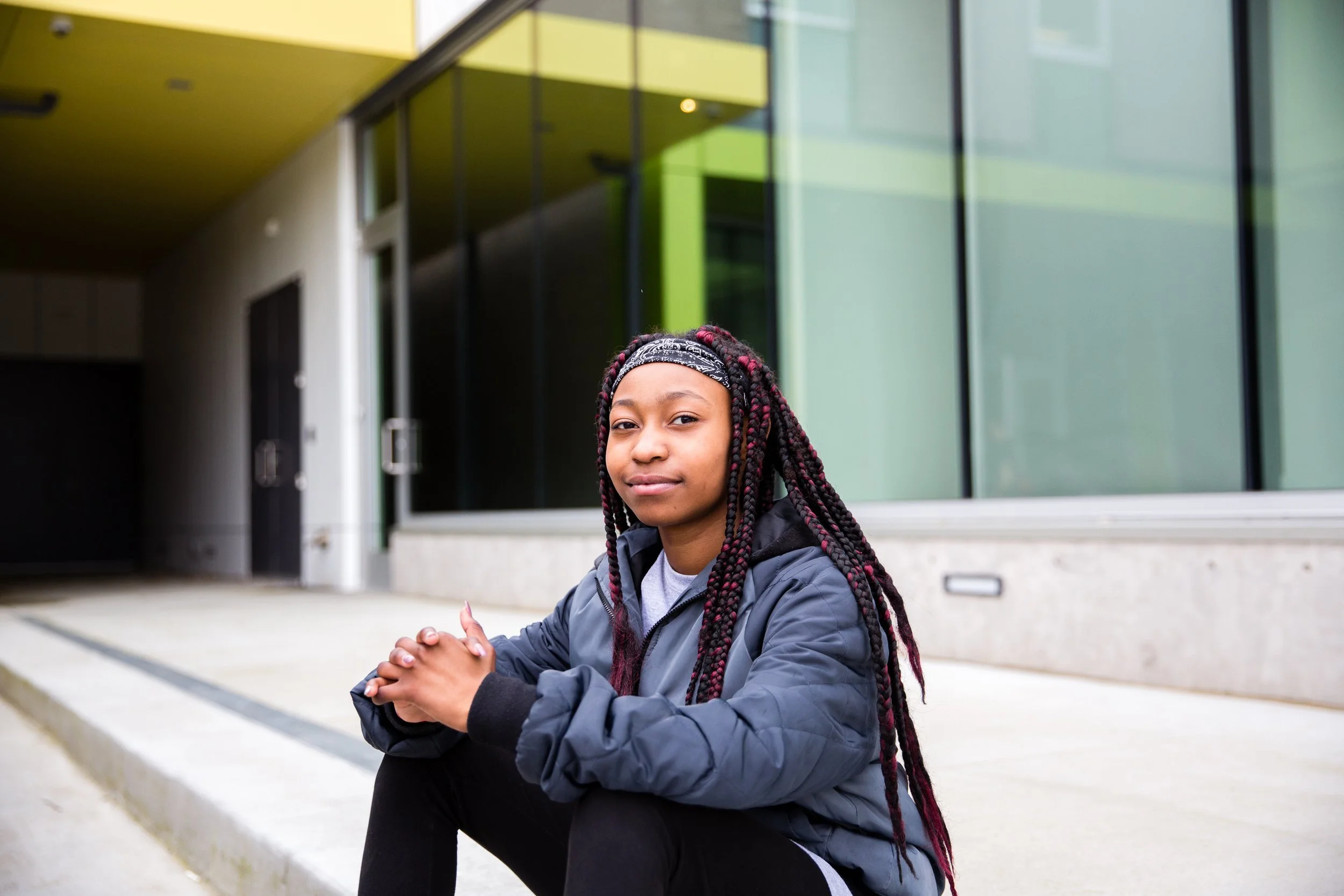 A Literacy Liberators student sitting outside a modern school building, smiling at the camera