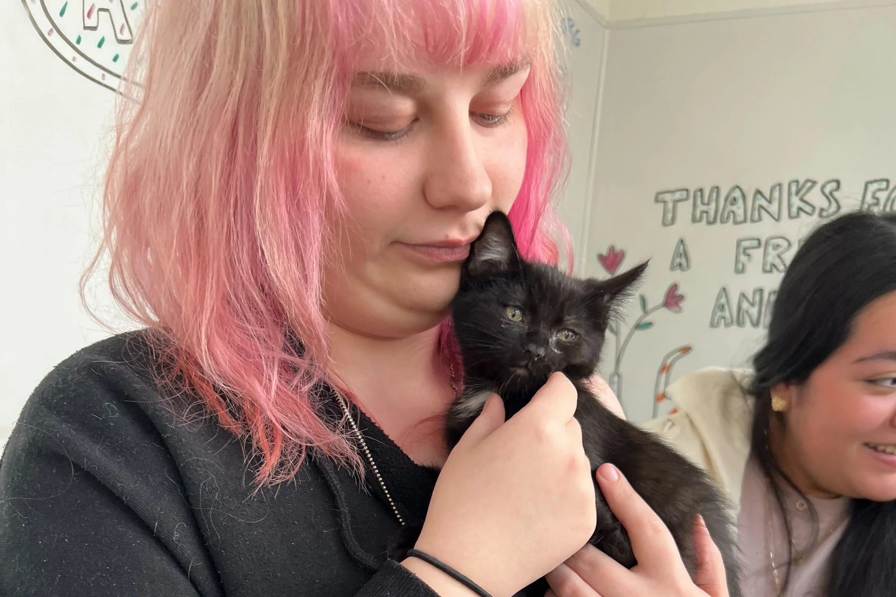 An Open School East staff member with pink hair holding a black kitten
