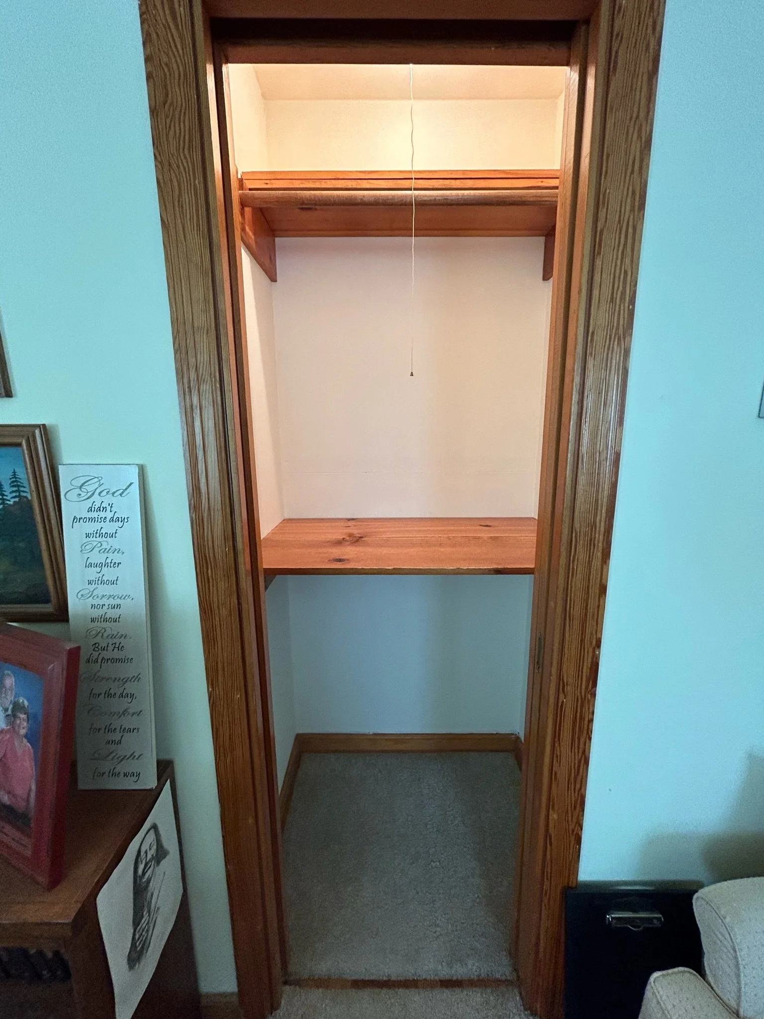 Empty wooden closet or cabinet with no contents, narrow inside, with a hanging cord from the ceiling for light or door mechanism.