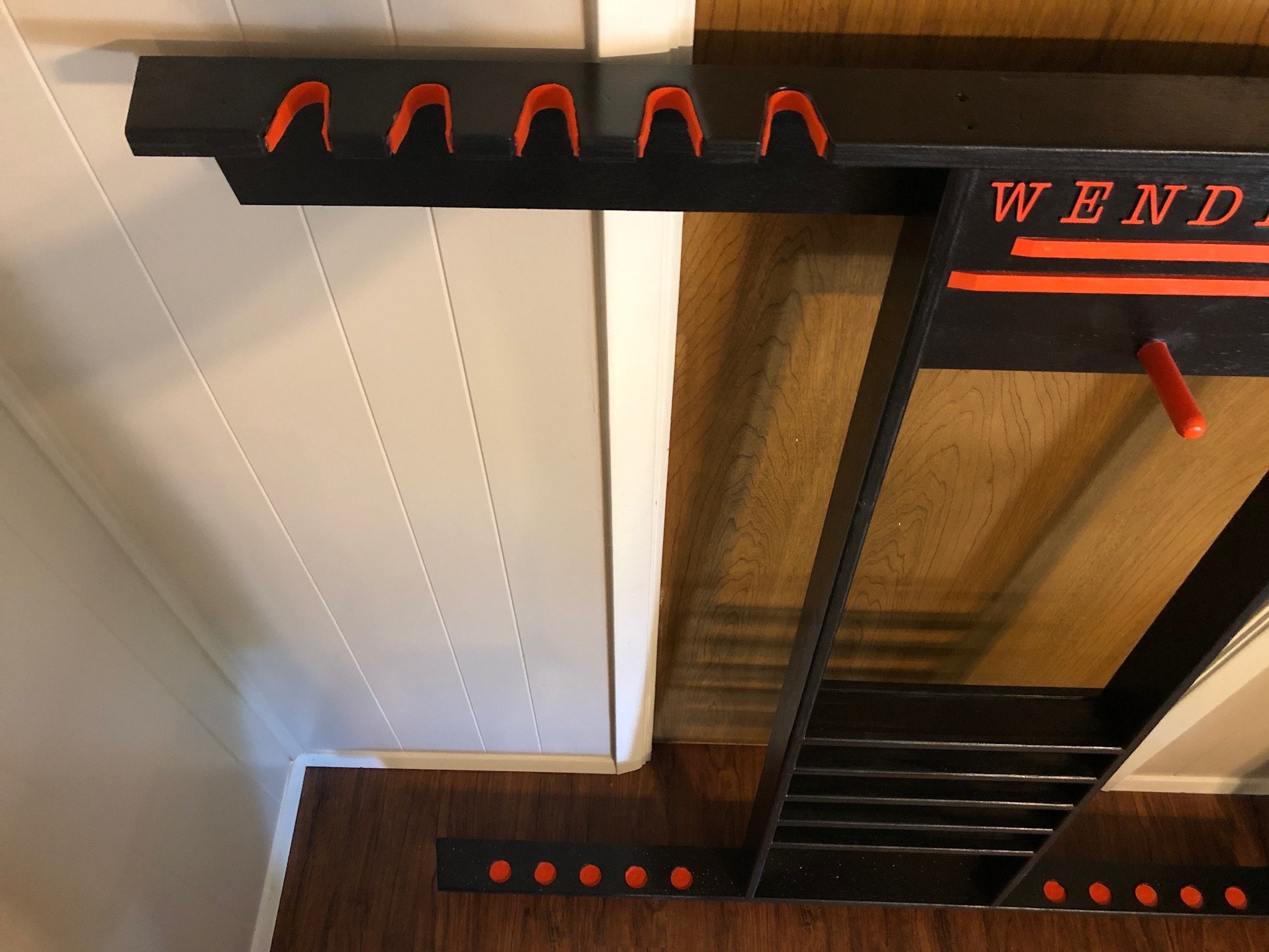 A black wooden rack with five orange hooks at the top and matching orange circular pegs at the bottom.