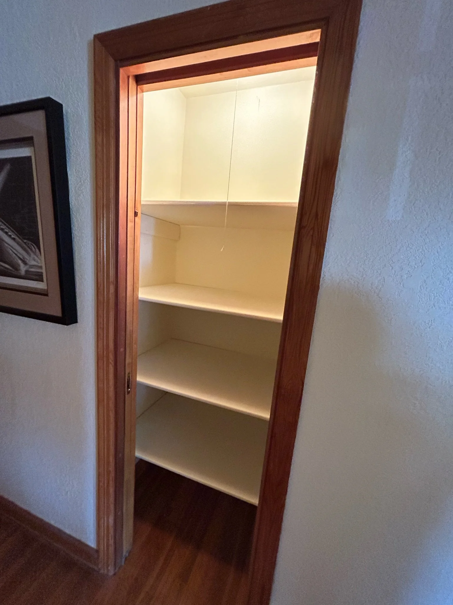 Empty wooden shelf with three levels inside a wooden closet or alcove, surrounded by beige walls.