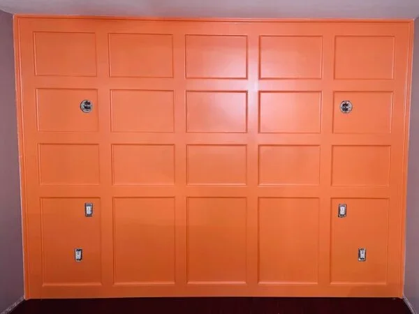 Orange garage door with panel design and four electrical outlets or switches.