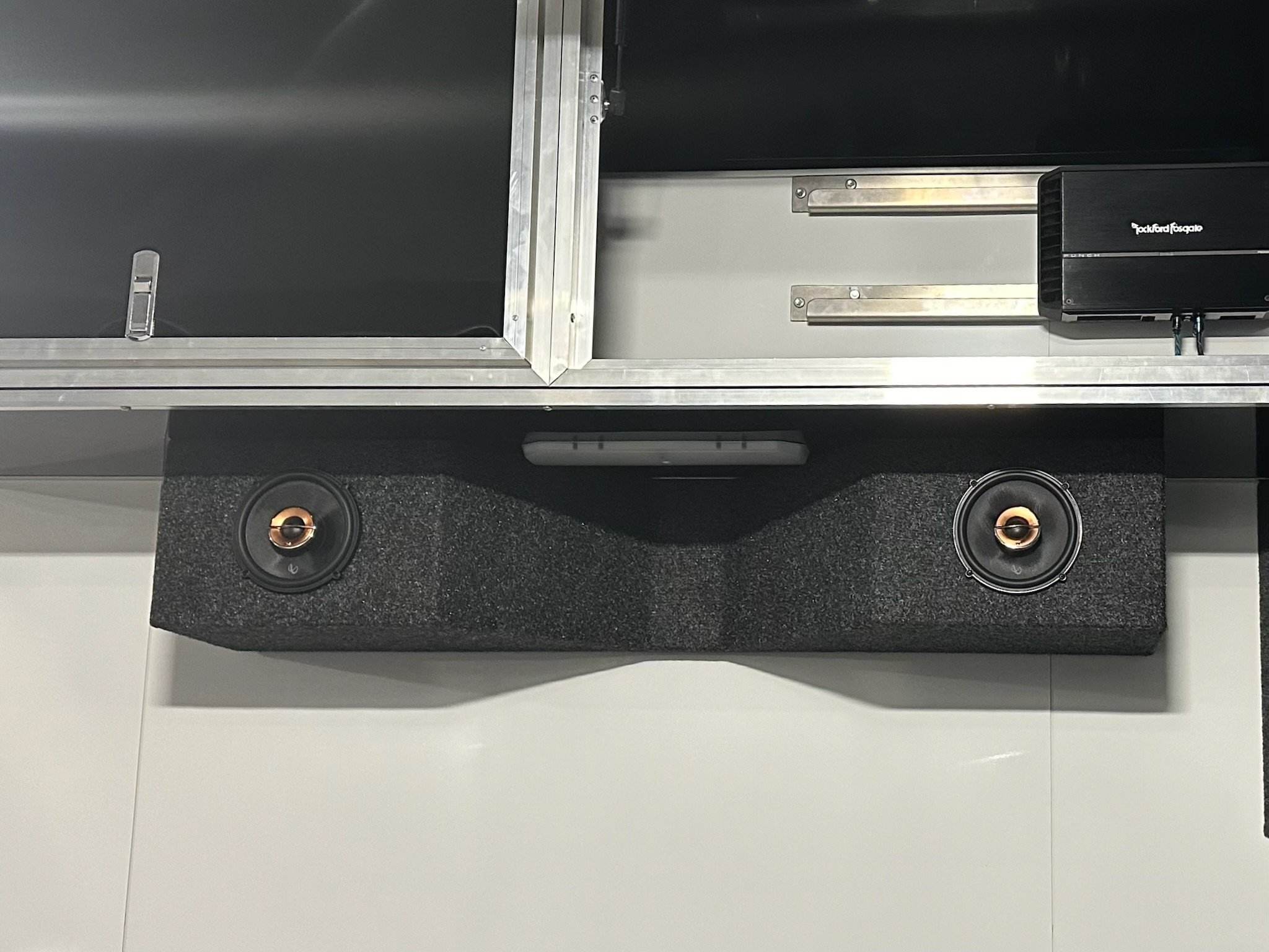 Close-up of audio equipment, showing two speakers with black cones and copper-colored centers, mounted on a black panel, with a gray and metallic casing possibly part of a larger sound system or speaker enclosure.