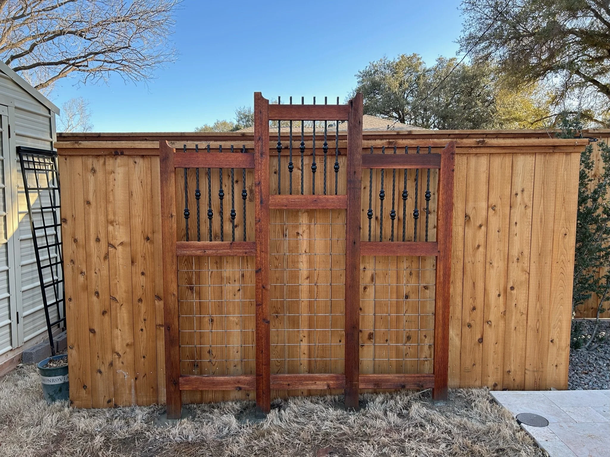A wooden fence with a gate, with a clear blue sky and trees in the background.