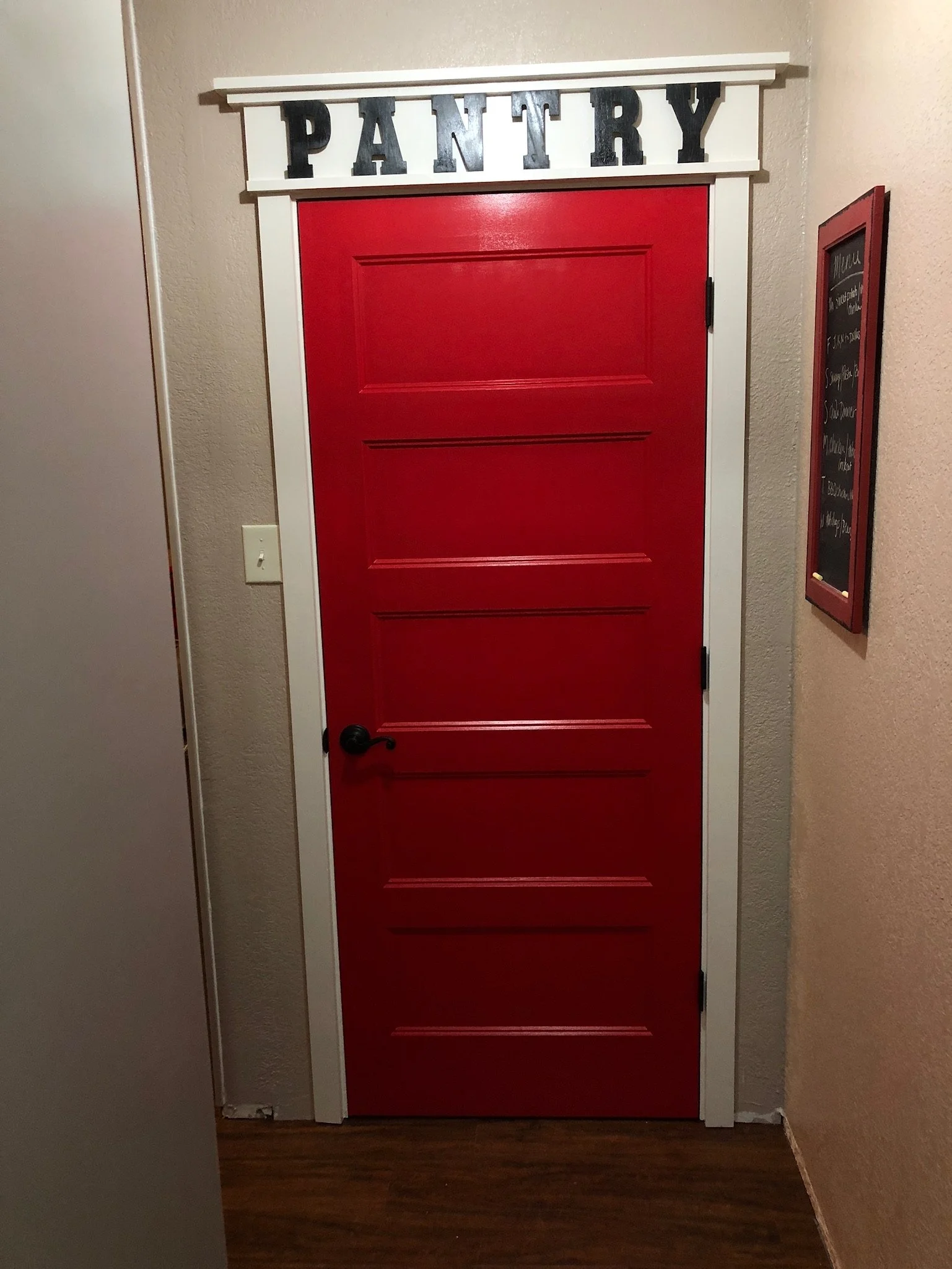 Red door with a white frame and black lettering sign above it that says 'PANTRY'.