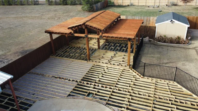 Overhead photo of a backyard deck under construction, with wooden beams and framing in place, and a partially built pergola with a slanted roof.