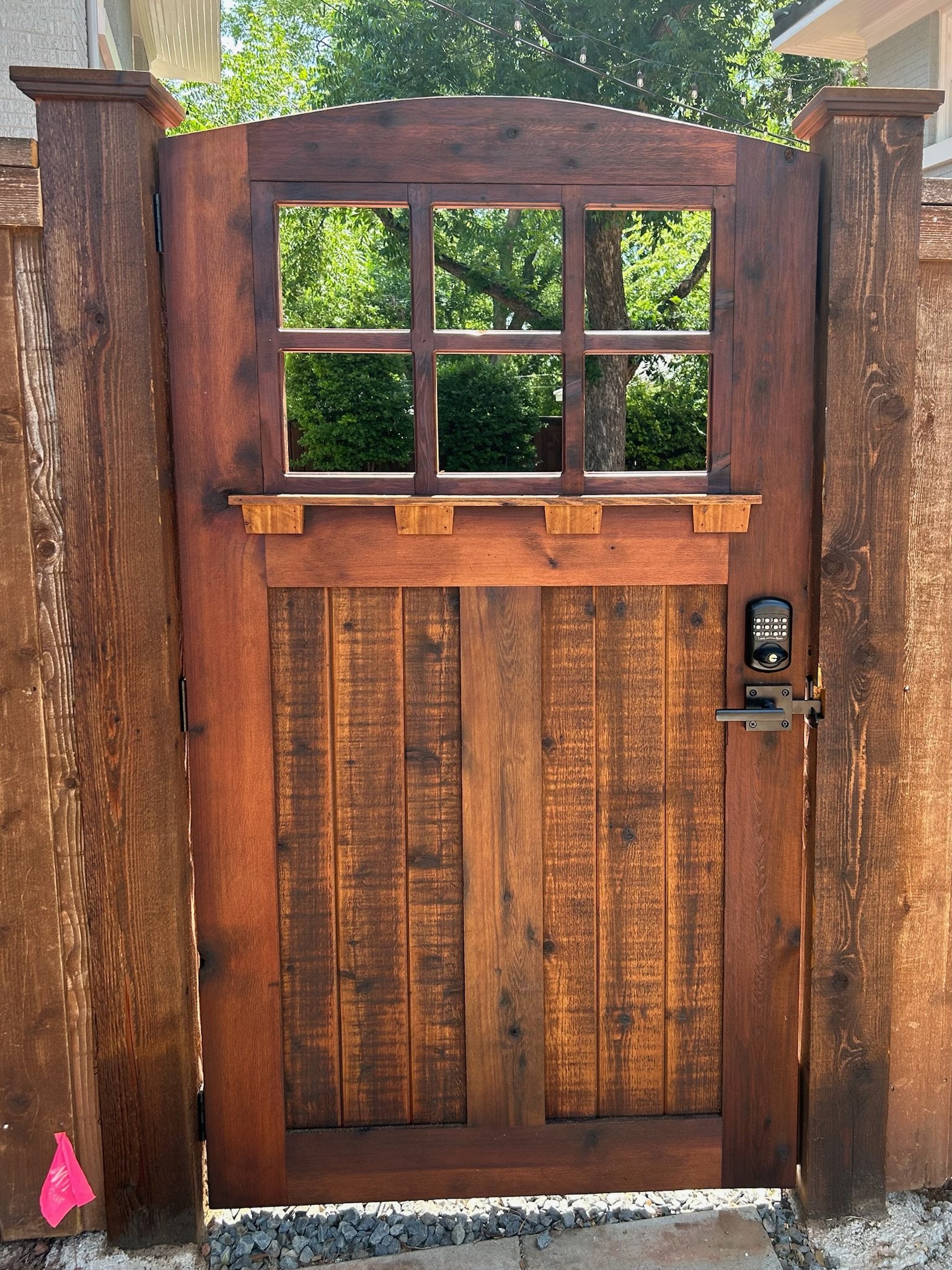 Wooden fence gate with window panes, electronic keypad lock, handle, and hinges, designed for residential entrance.