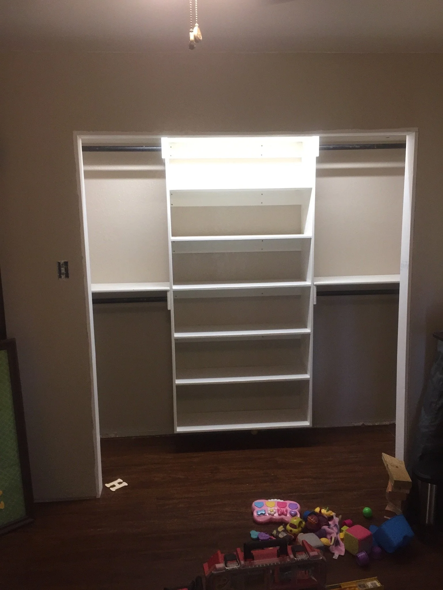 A white-framed empty closet with beige walls and hardwood floor, with scattered toys on the floor below.