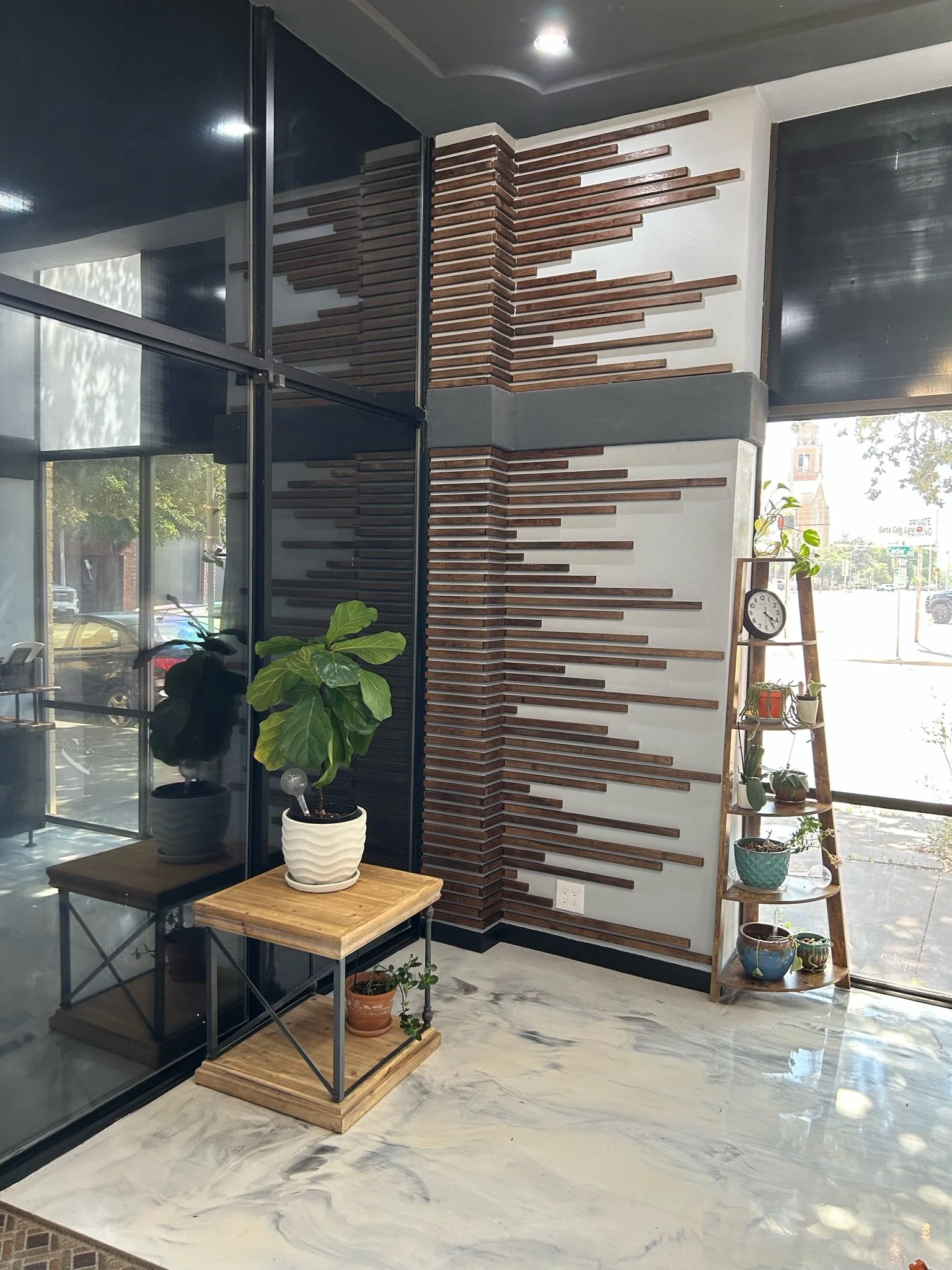 Interior of a modern space with a decorative wood slat accent wall, a large glass window, and shelves with potted plants. Marble flooring enhances the contemporary design.