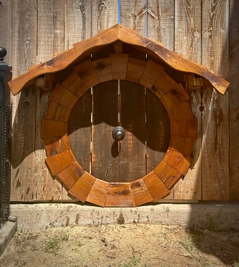 A wooden door with a decorative circular wooden frame and a small overhanging roof, set in a wooden fence.