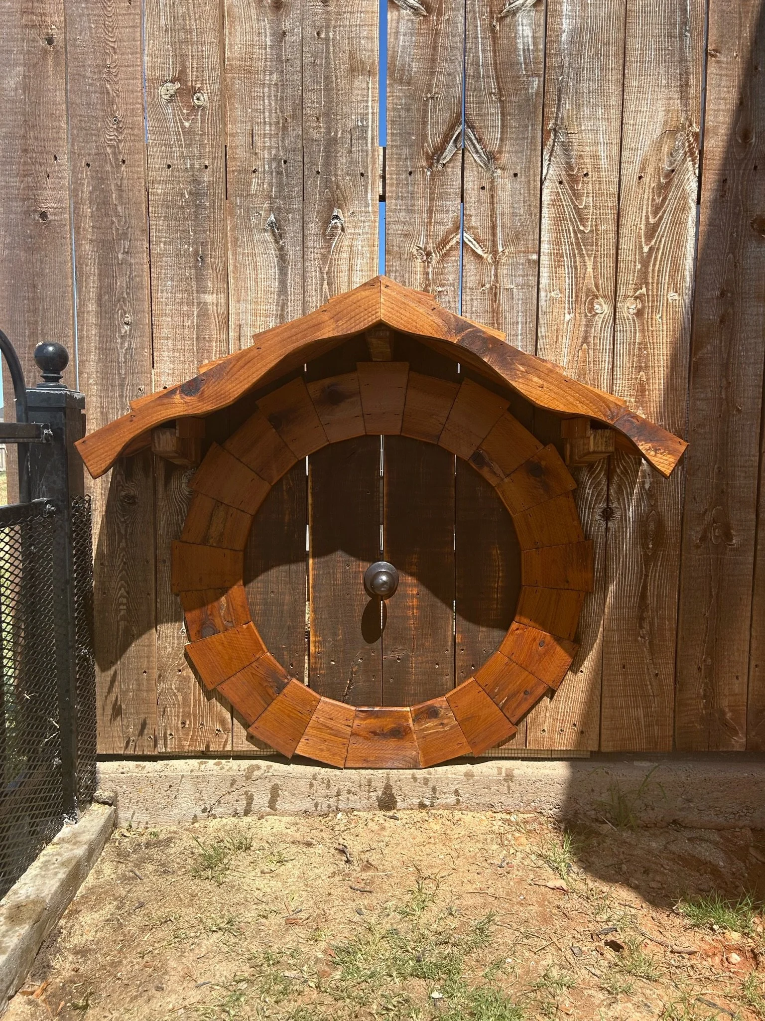 A large wooden clock frame with no clock hands mounted on a wooden fence.
