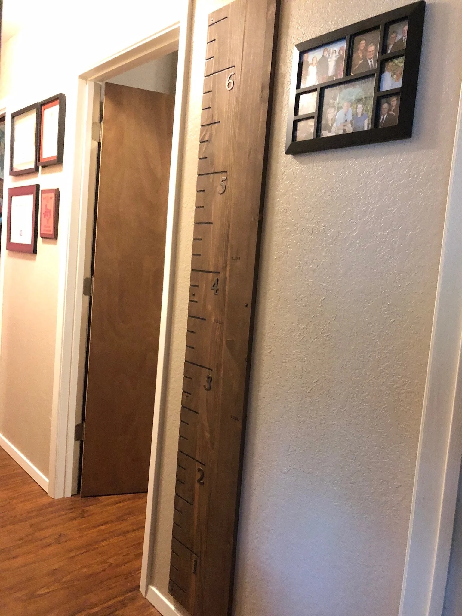 A wooden height measurement ruler with black numbers and lines, mounted vertically on a beige textured wall in a home interior.
