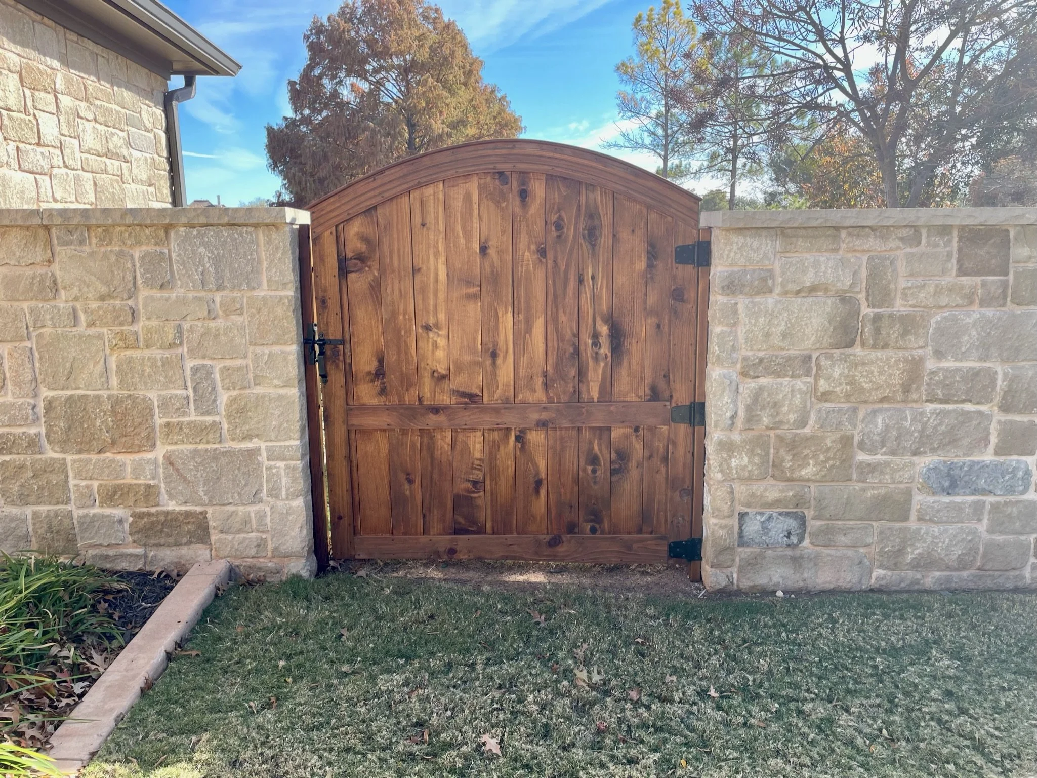 A wooden gate set into a stone wall, with trees in the background and a grassy lawn in the foreground.