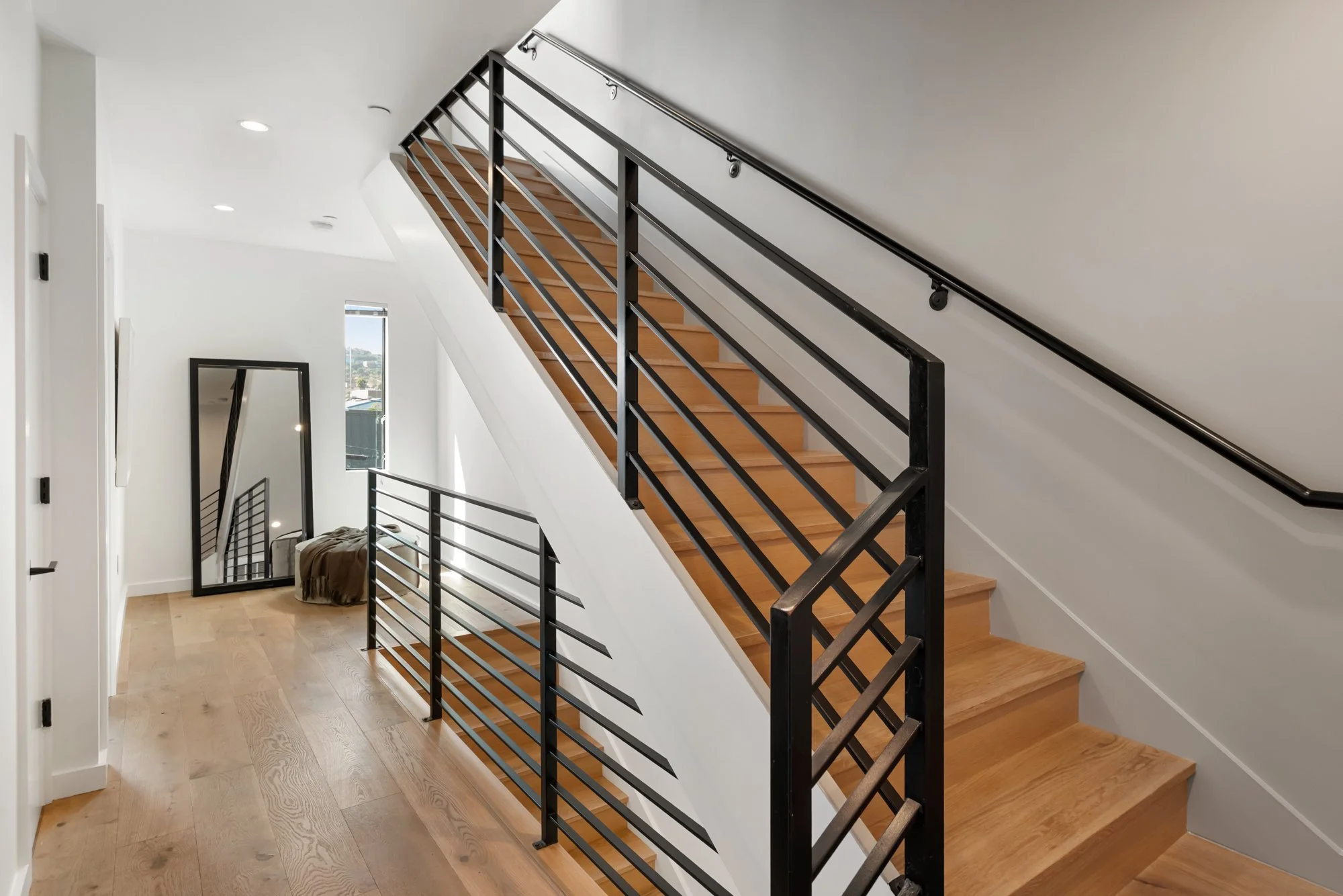 Modern staircase with wooden steps and a black metal railing inside a bright, white-walled home.