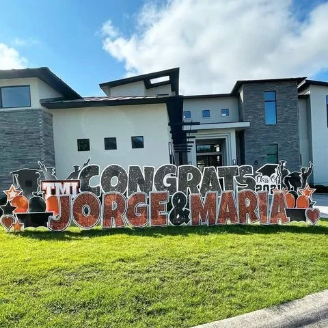 Large outdoor congratulatory sign for Jorge and Maria in front of a modern house with a green lawn.