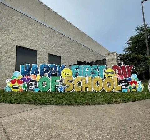Colorful sign outside a building celebrating the first day of school with emojis and cheerful messages.