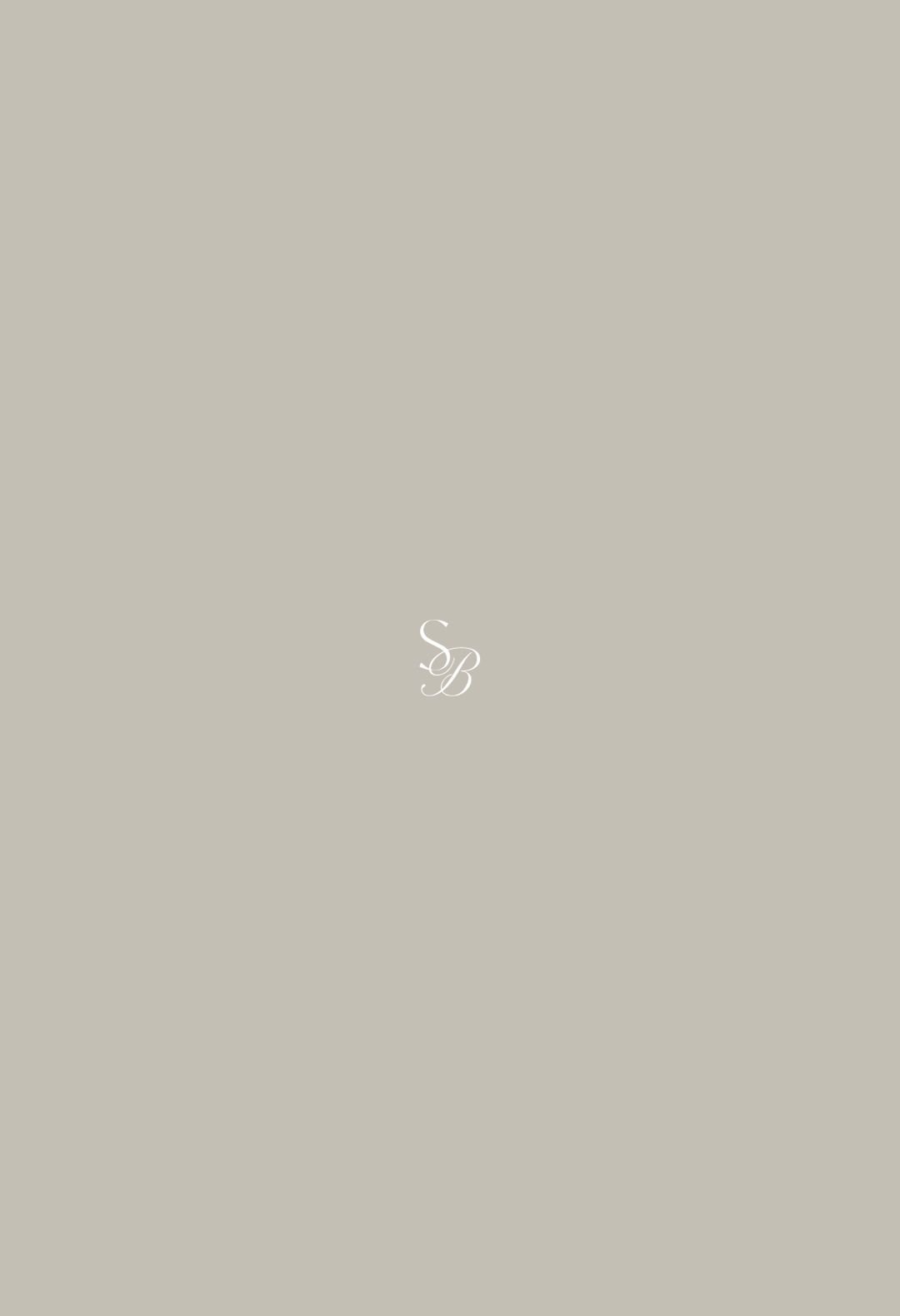 A minimalist beige background with a small, elegant white monogram of the letters 'SB' in the center.