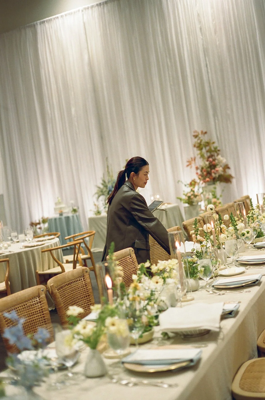 A woman in a gray blazer standing at a beautifully decorated banquet table with floral arrangements and candles in an elegant event space.