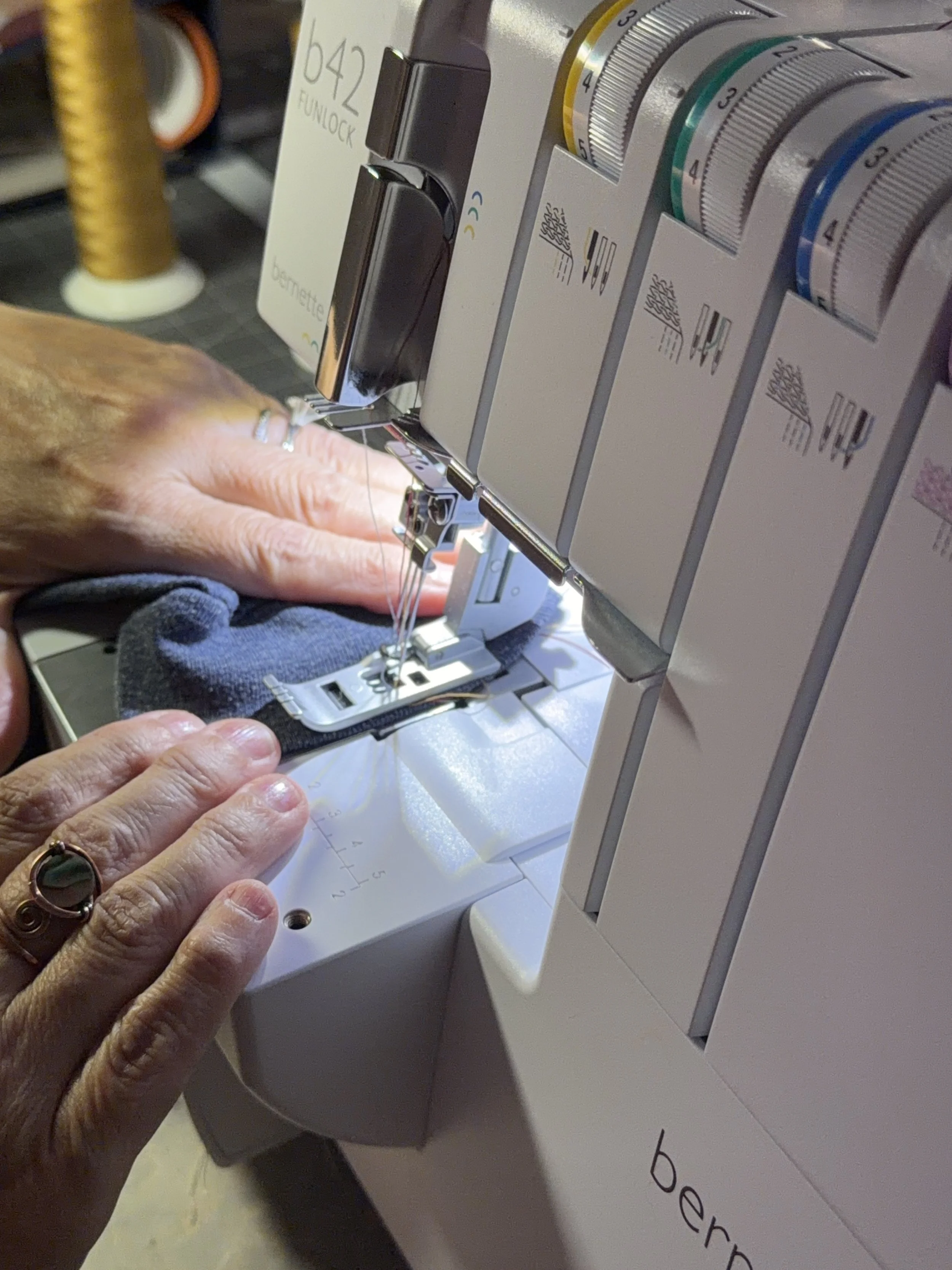 Close-up of a person's hand guiding a piece of black fabric with a sewing machine, with the person's fingers near the needle.