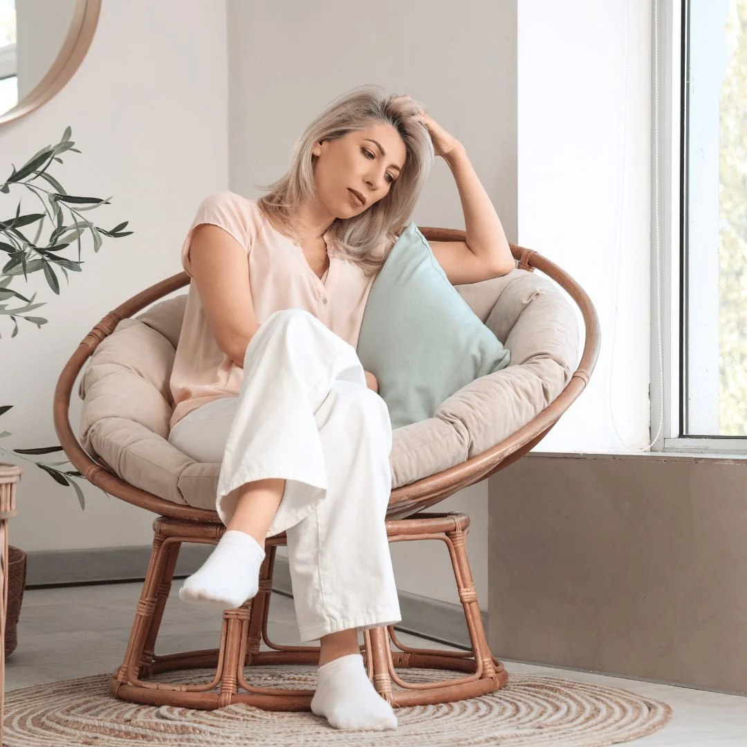 Woman resting in a chair with her hand on her head, feeling the fatigue that can come with perimenopause