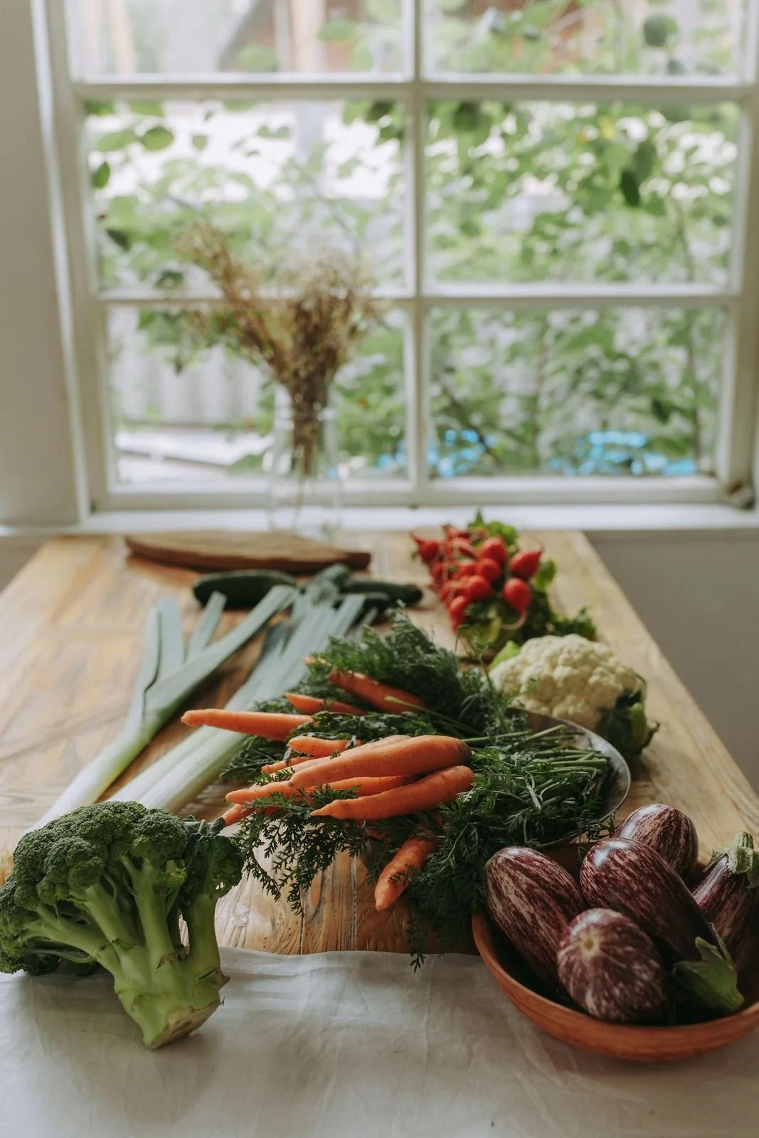 Fresh vegetables and greens on a wooden table by a sunny window