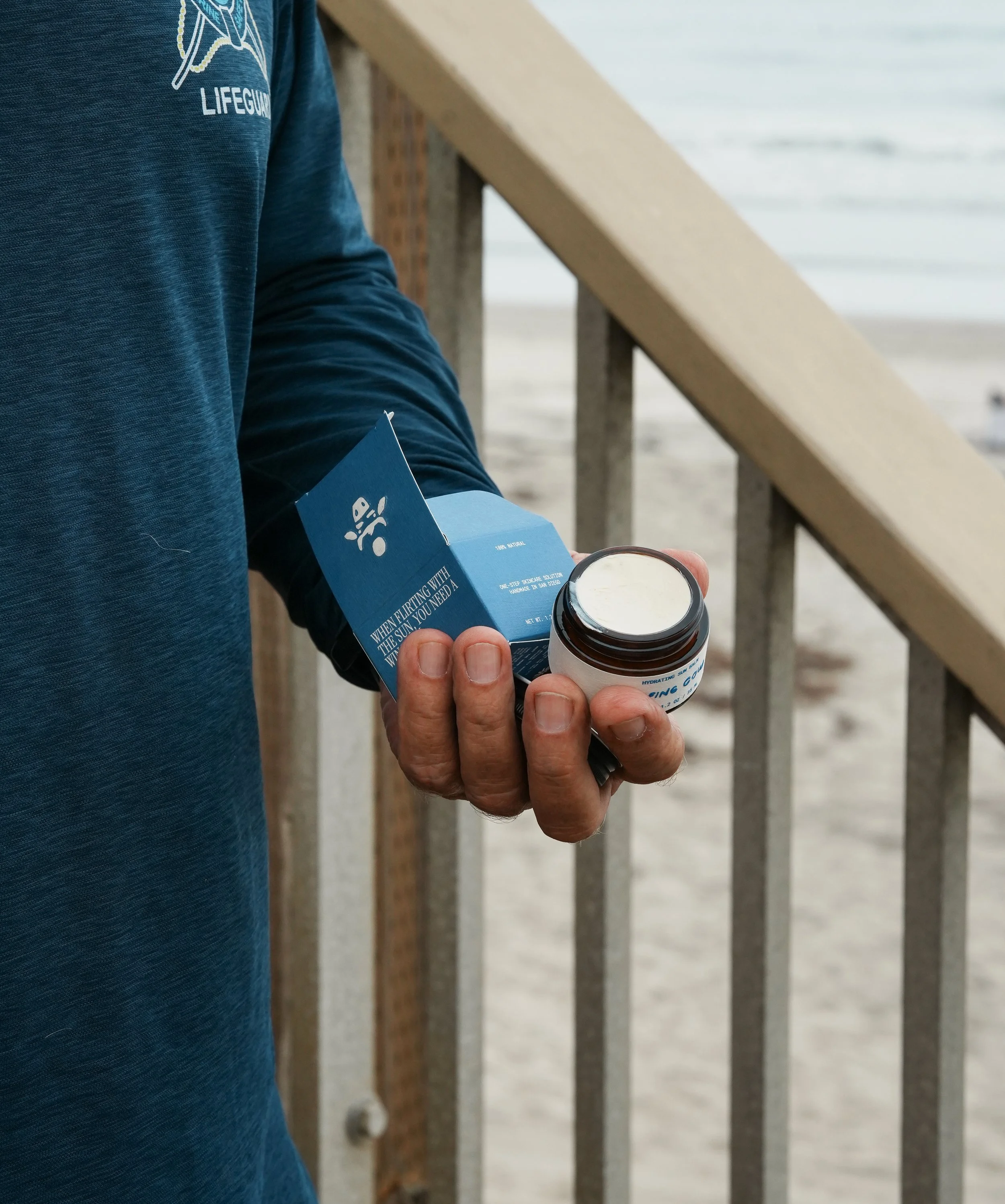 Person holding a blue informational brochure and a small brown bottle on a beach boardwalk.