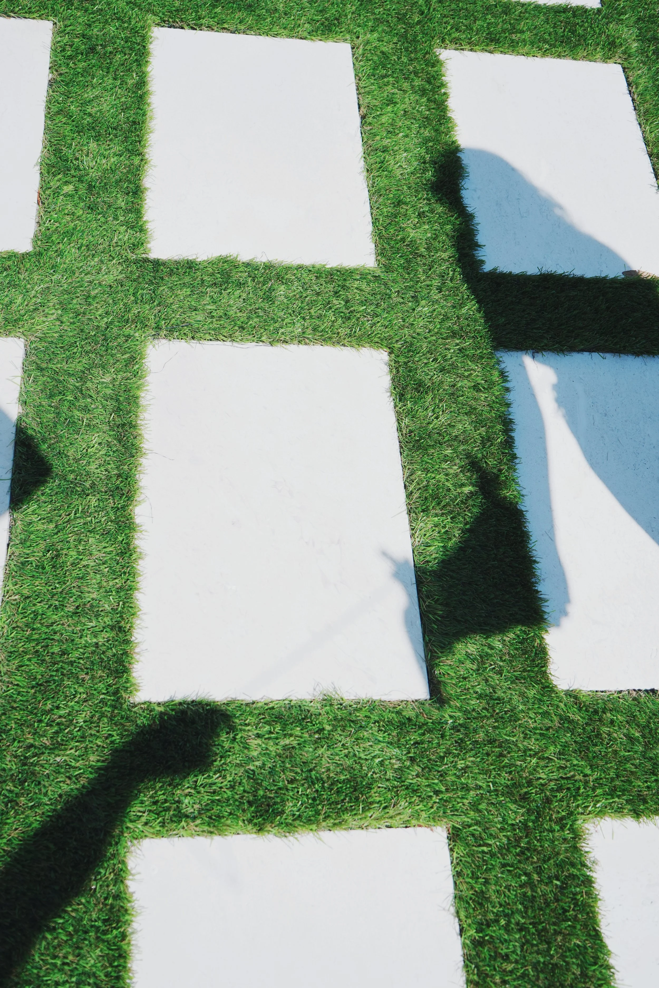Square concrete tiles separated by green grass in a geometric pattern.