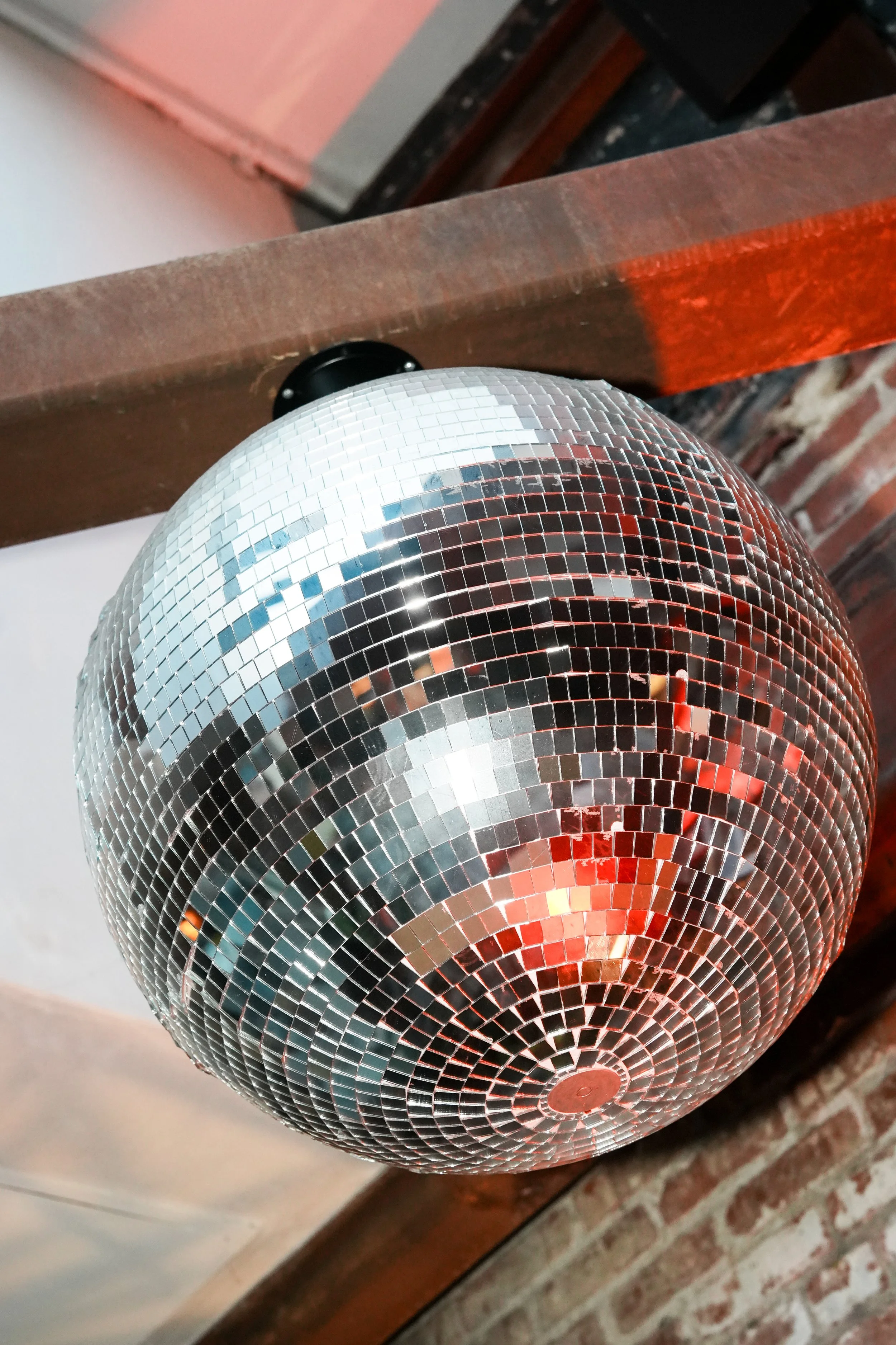 Close-up of a disco ball hanging in a corner near brick wall and wooden furniture with a pink-painted wall in the background.