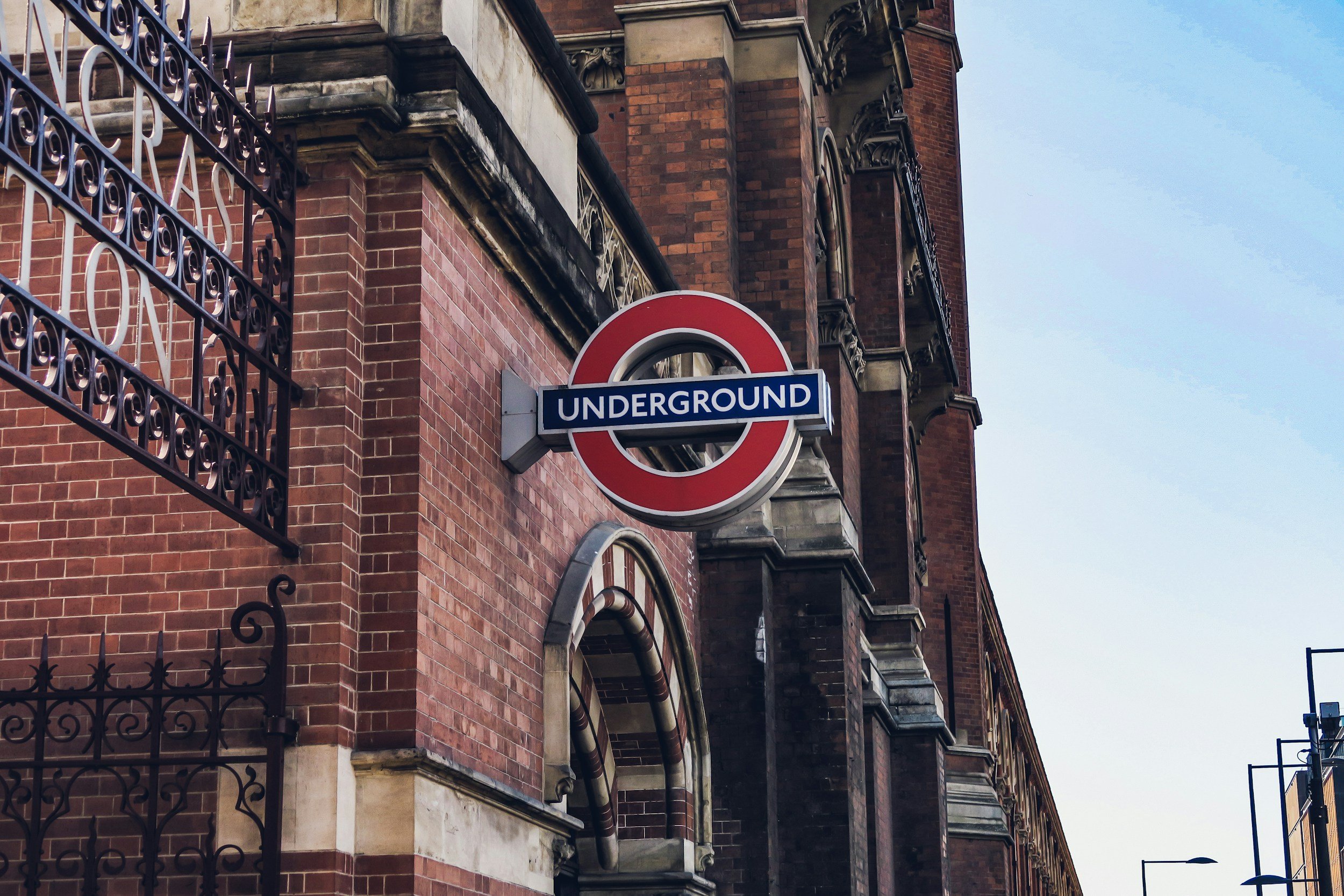 An urban street scene featuring a brick building with ornate windows, a fire escape, and a street sign for the London Underground.