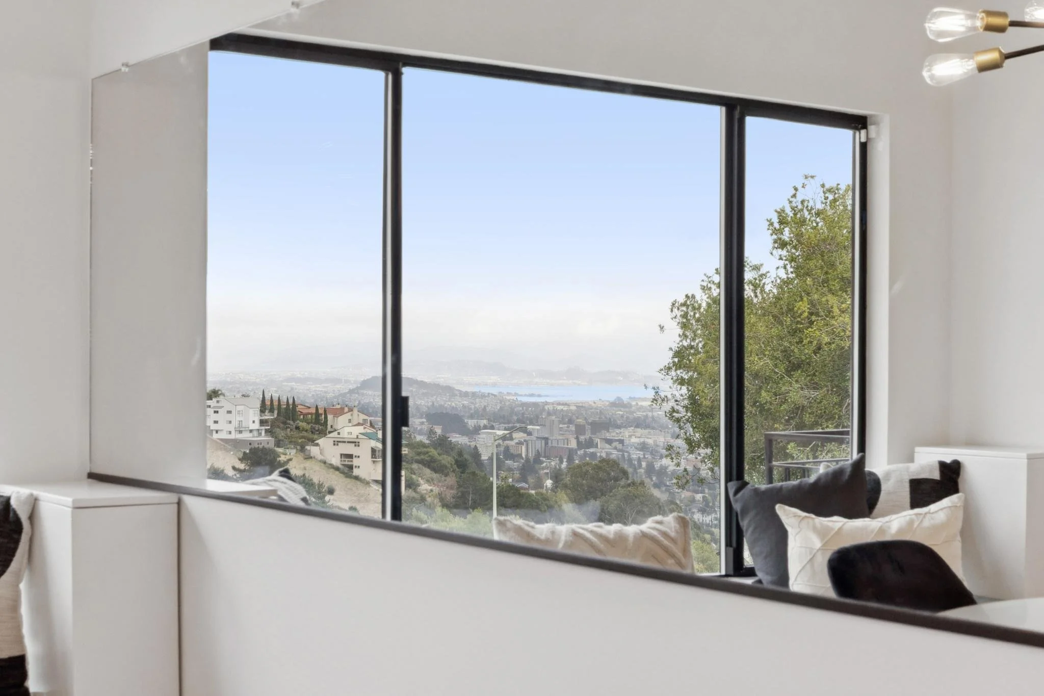 Reflection in a mirror showing a view of a cityscape through large windows, with trees and buildings.