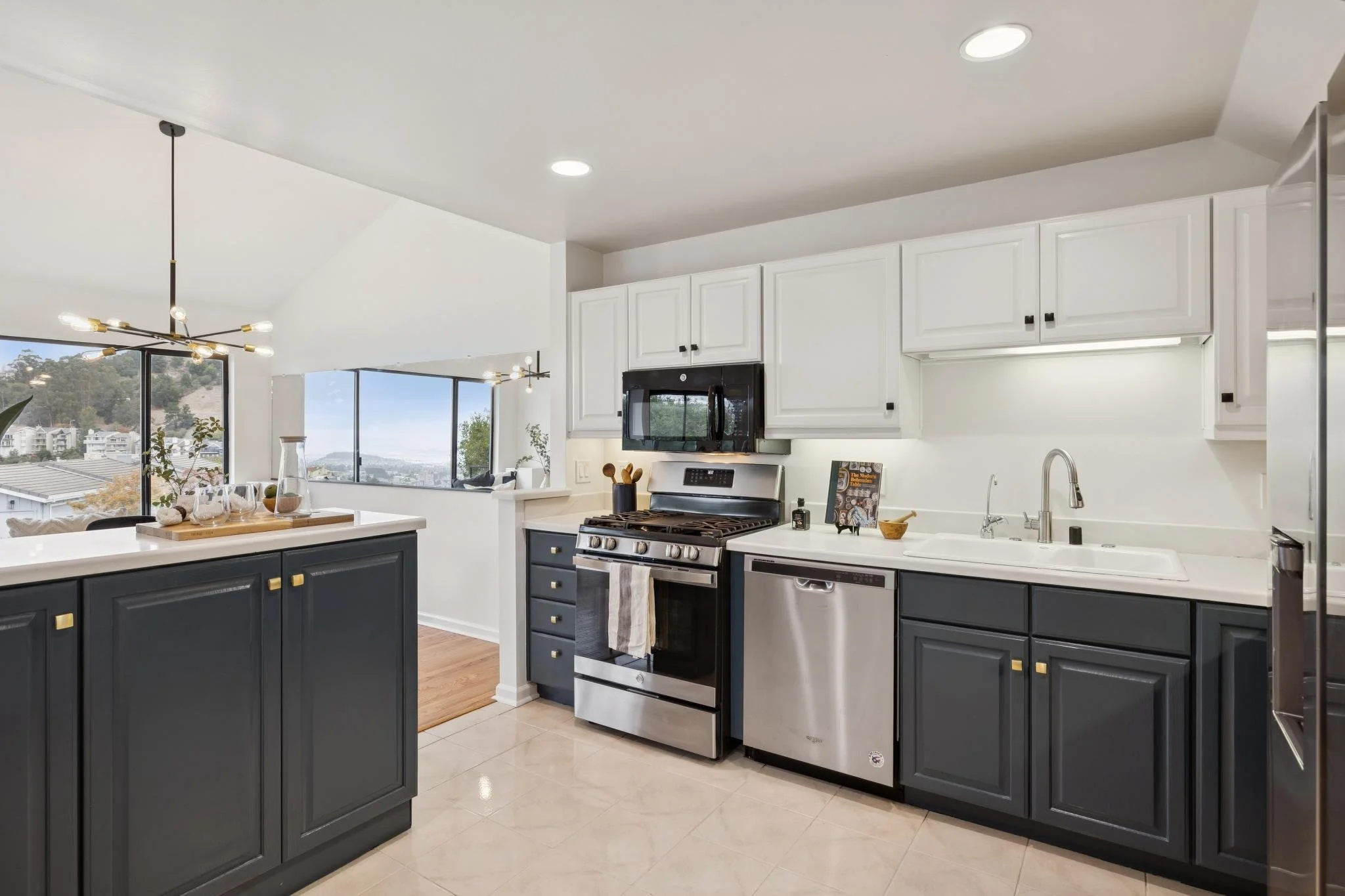 Modern kitchen with white cabinets, stainless steel appliances, black lower cabinets, and a view of large windows with a scenic view outside.